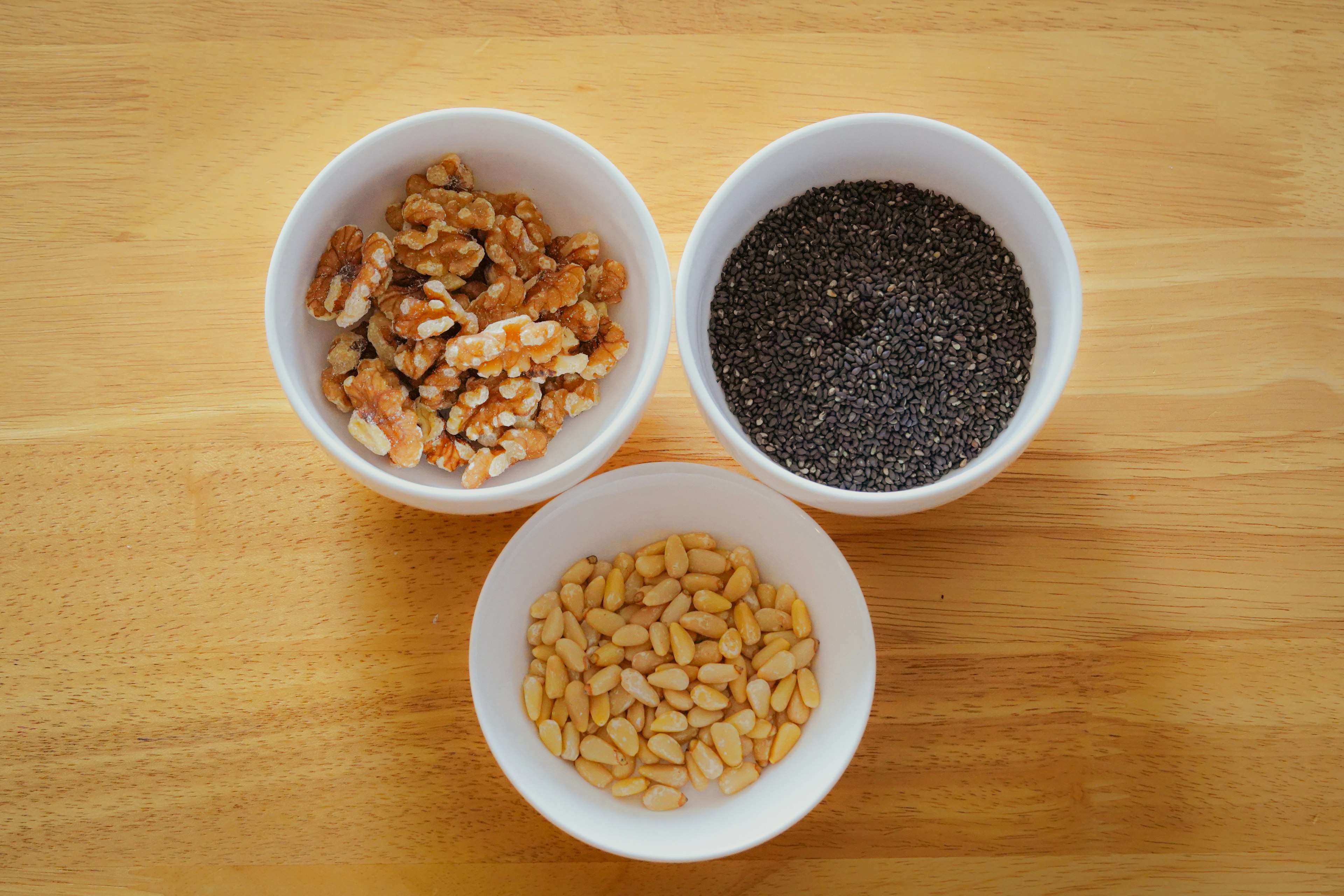 White bowls containing walnuts, chia seeds, and peanuts on a wooden table