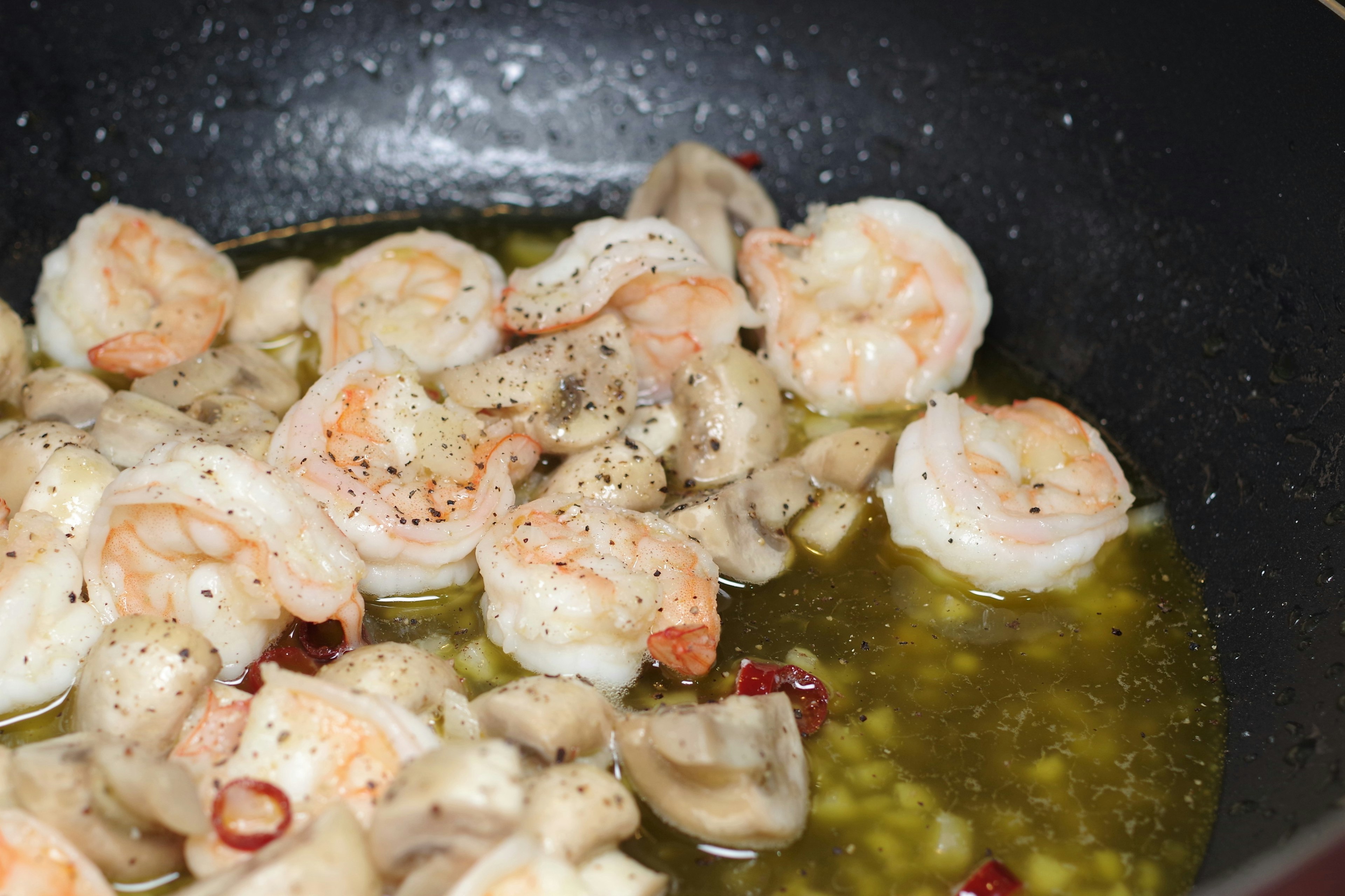 Shrimp and mushrooms sautéing in a pan with olive oil