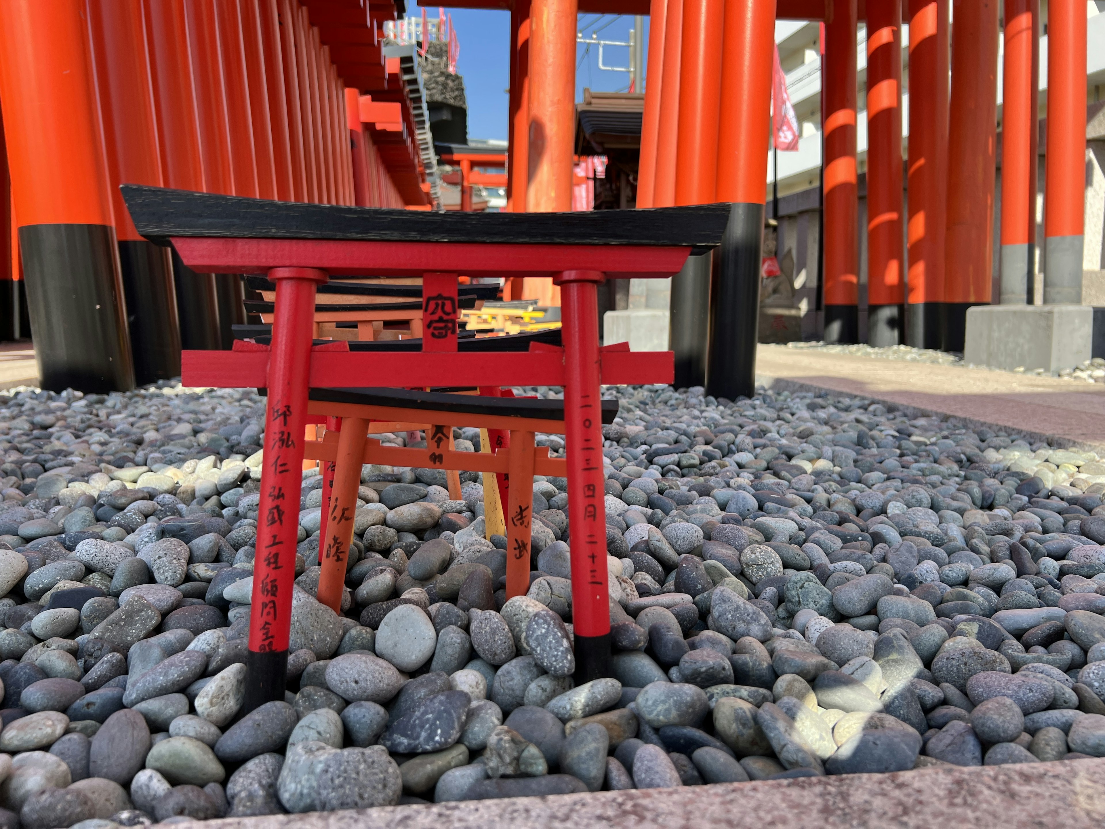 Small red chair in front of red torii gates with pebbled ground