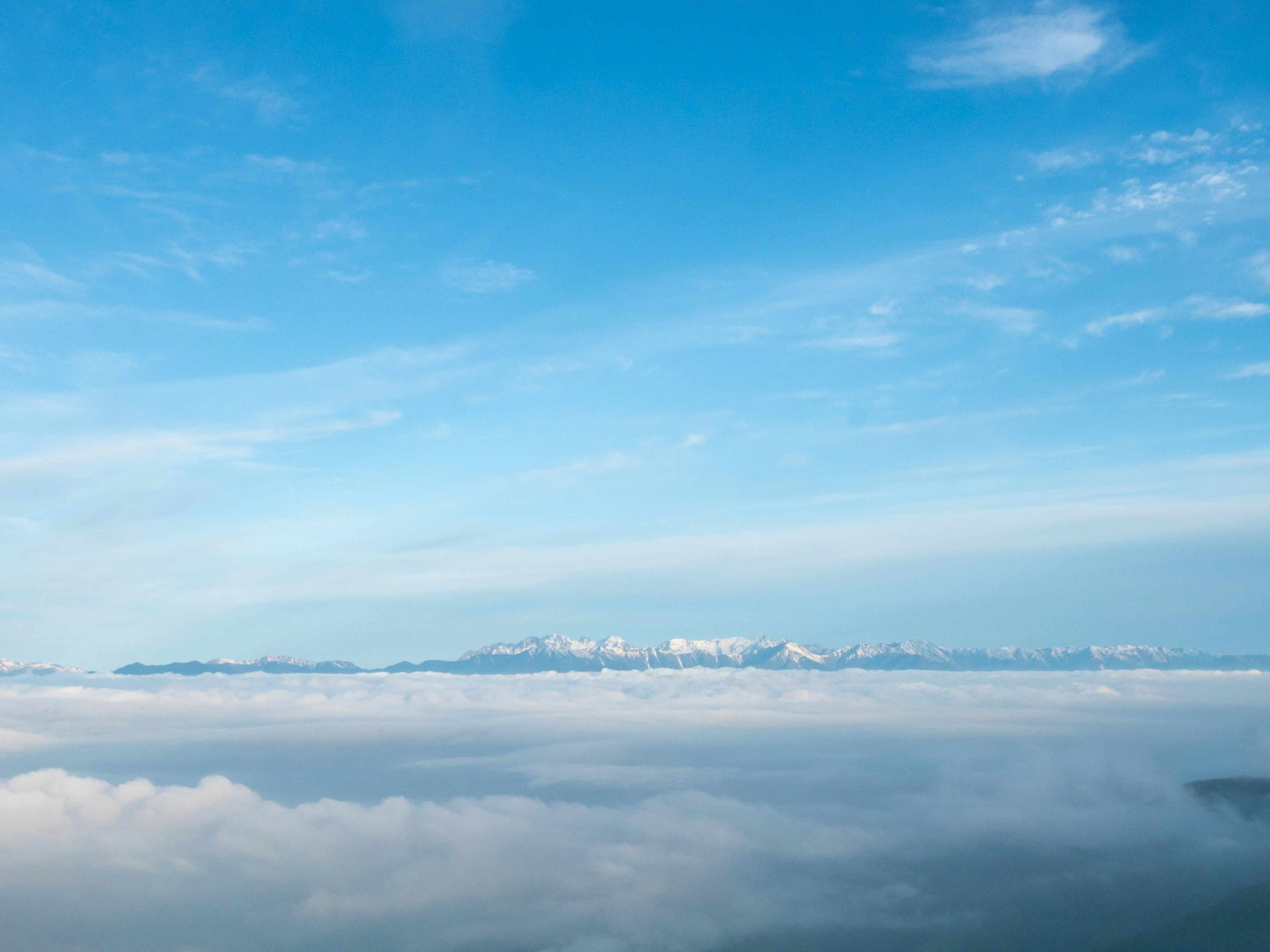 Montañas cubiertas de nieve sobre un mar de nubes bajo un cielo azul