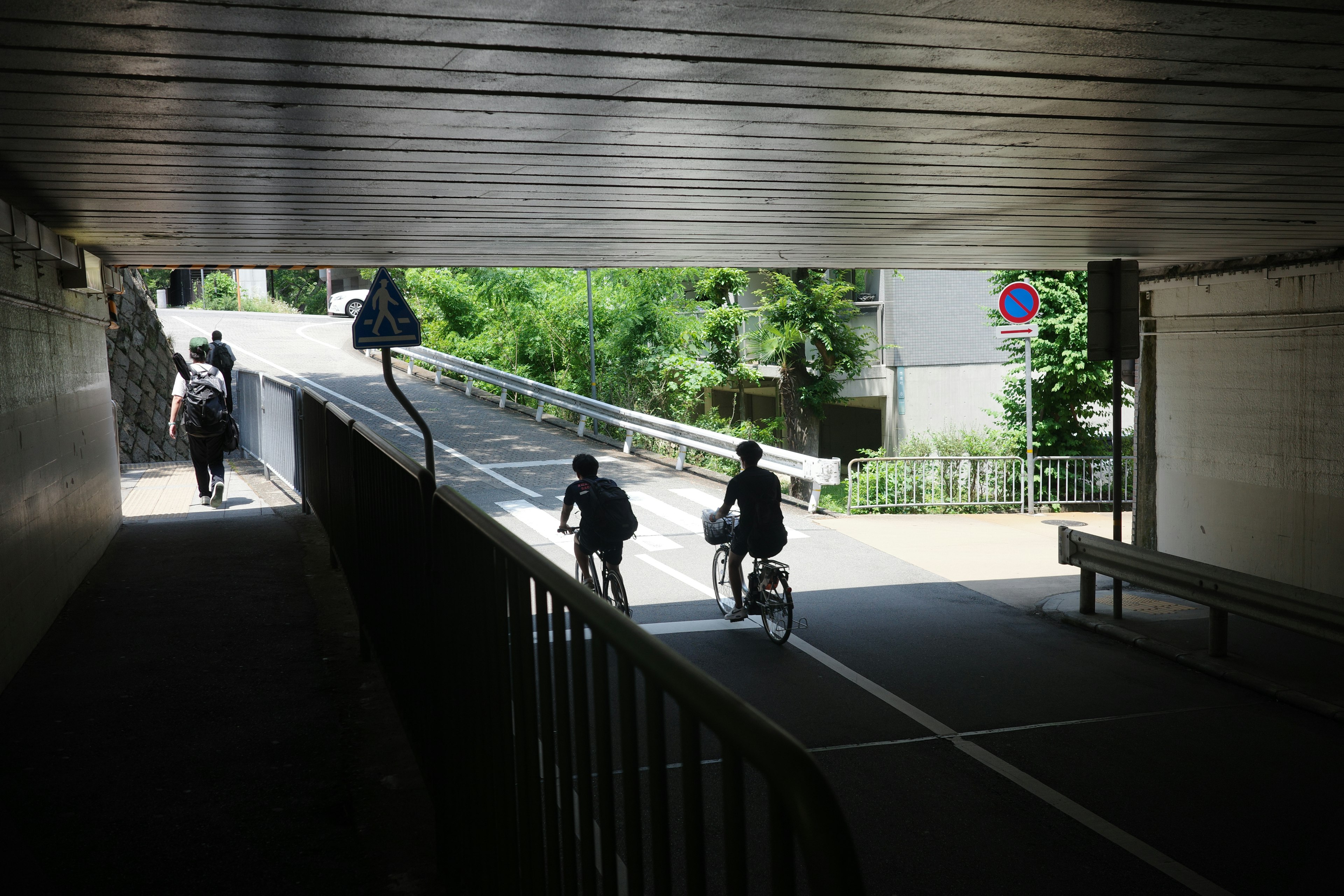 A cyclist and a pedestrian exiting a tunnel onto a sunny road