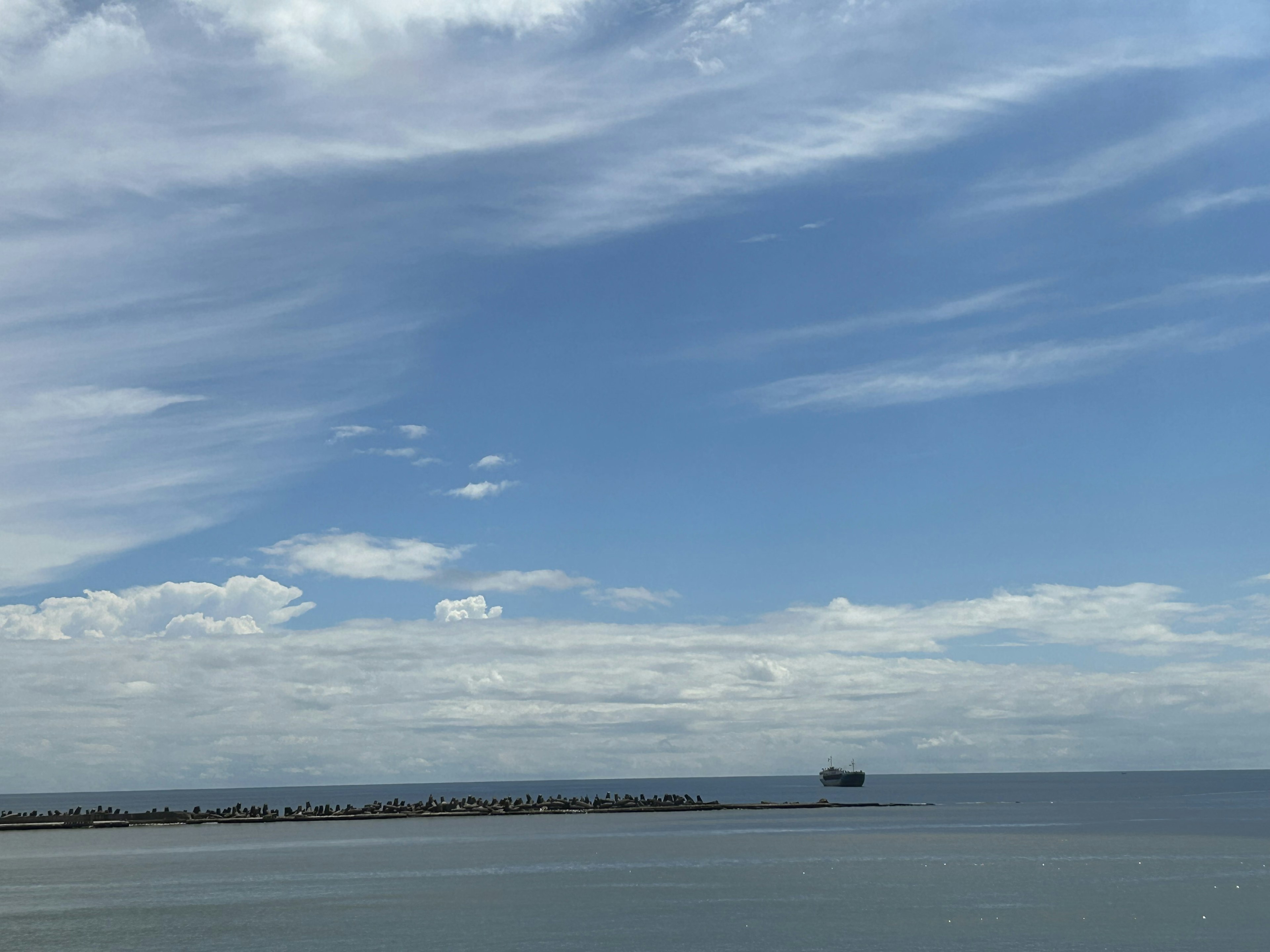 青い空と雲の下に静かな海が広がり小さな船が見える風景