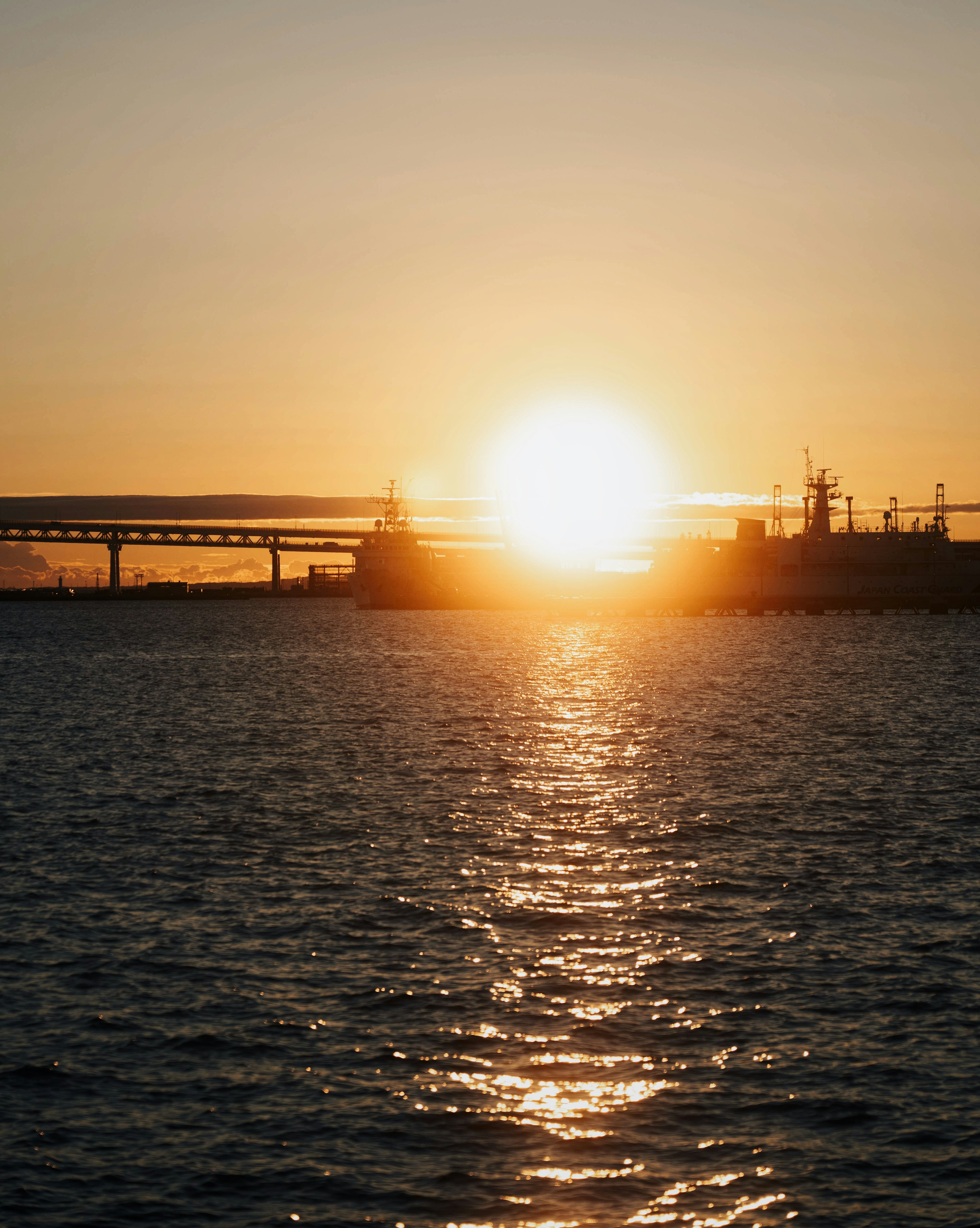 港口景色，夕陽映照在水面上，有船隻和橋樑