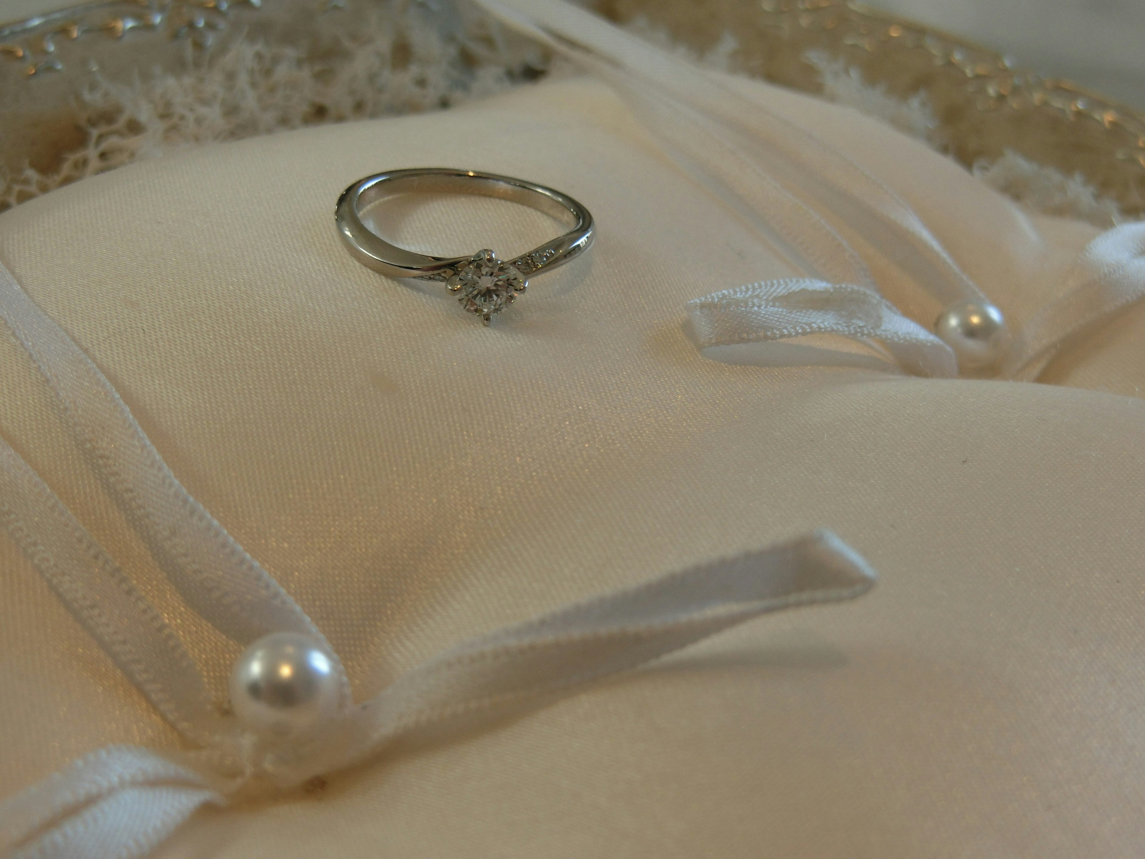 Wedding ring placed on a cushion with ribbons and pearls