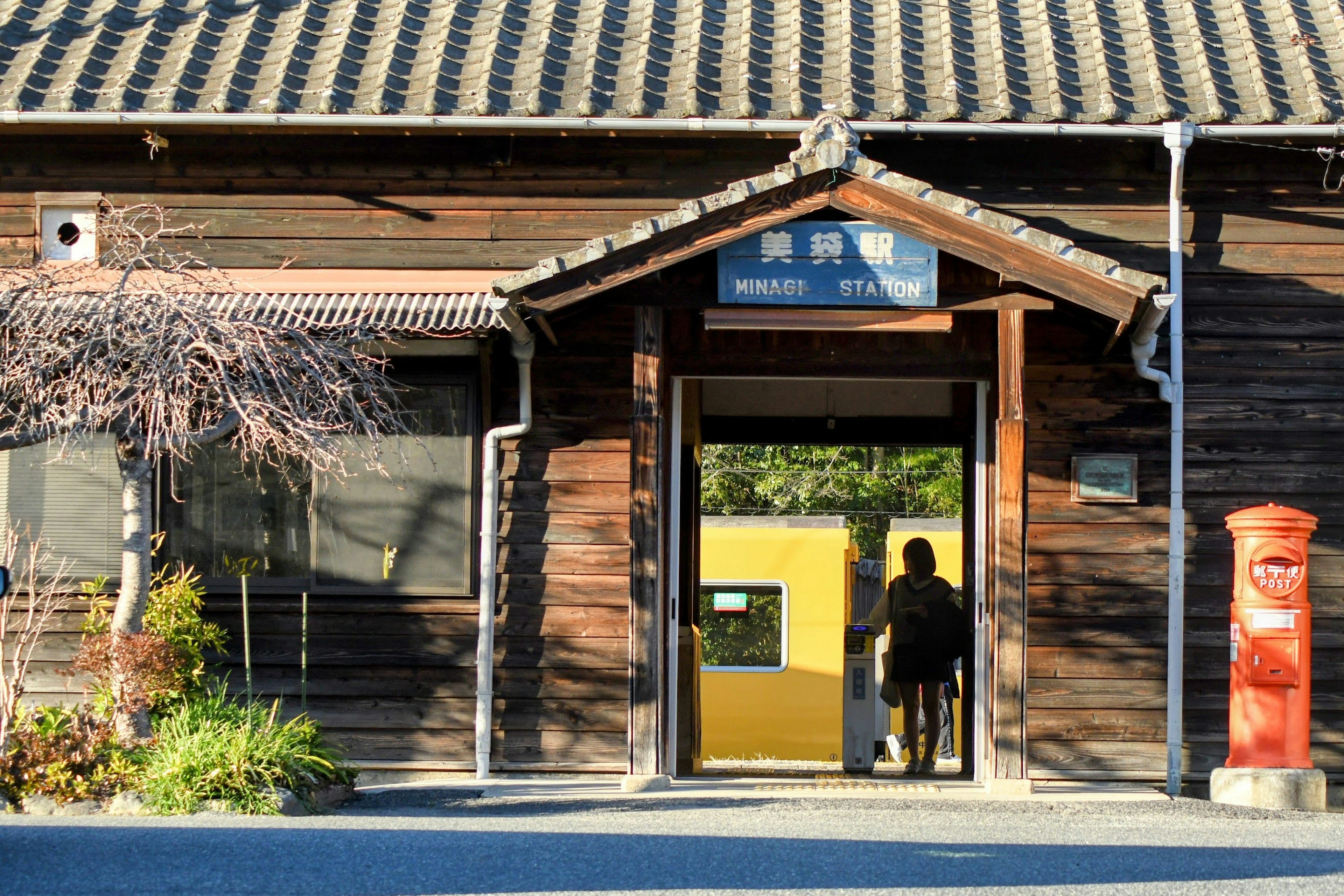 Silhouette of a person standing at the entrance of a wooden station building with green plants around