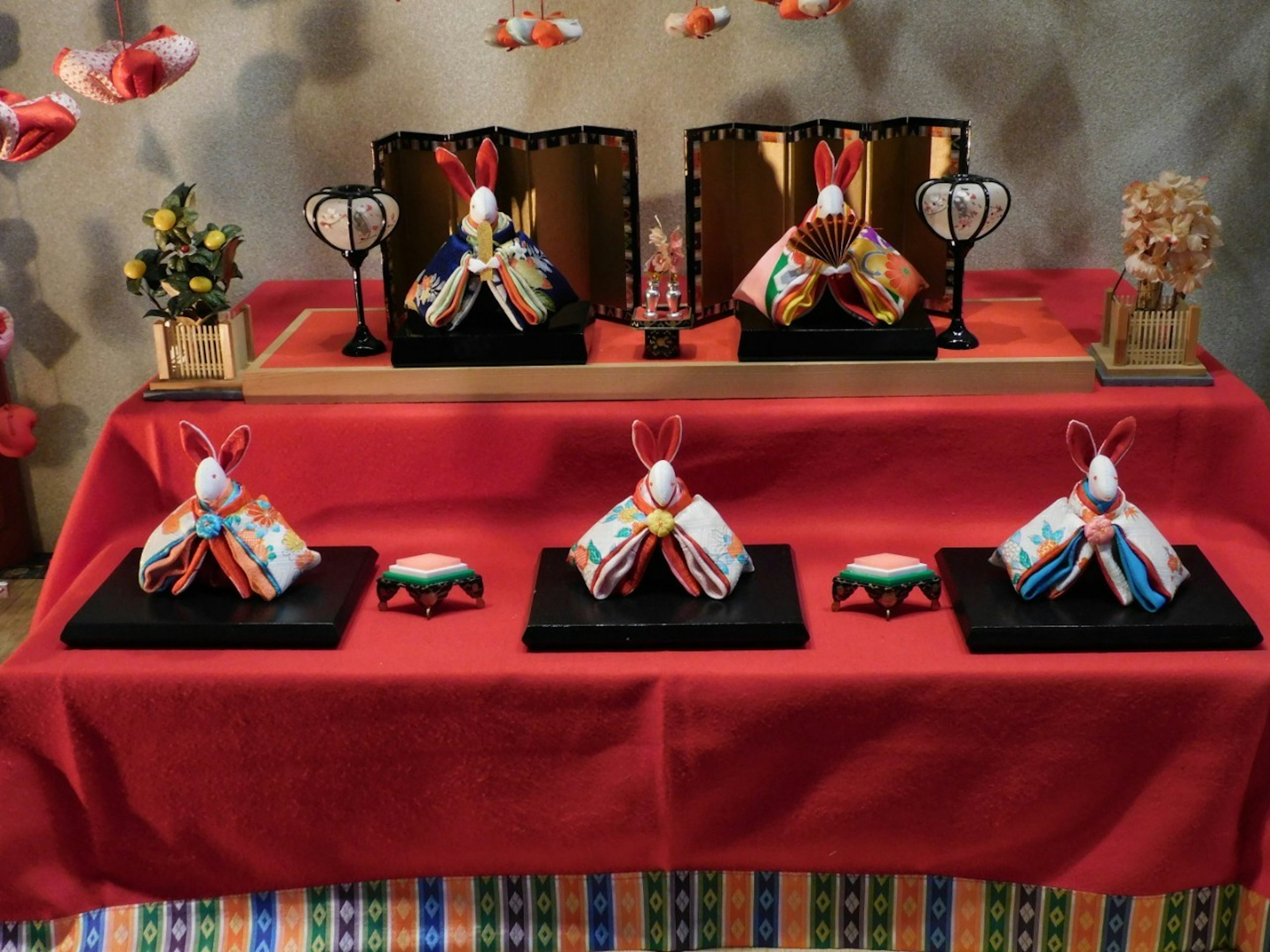 Exhibición de muñecas hina tradicionales en una mesa roja con arreglos florales