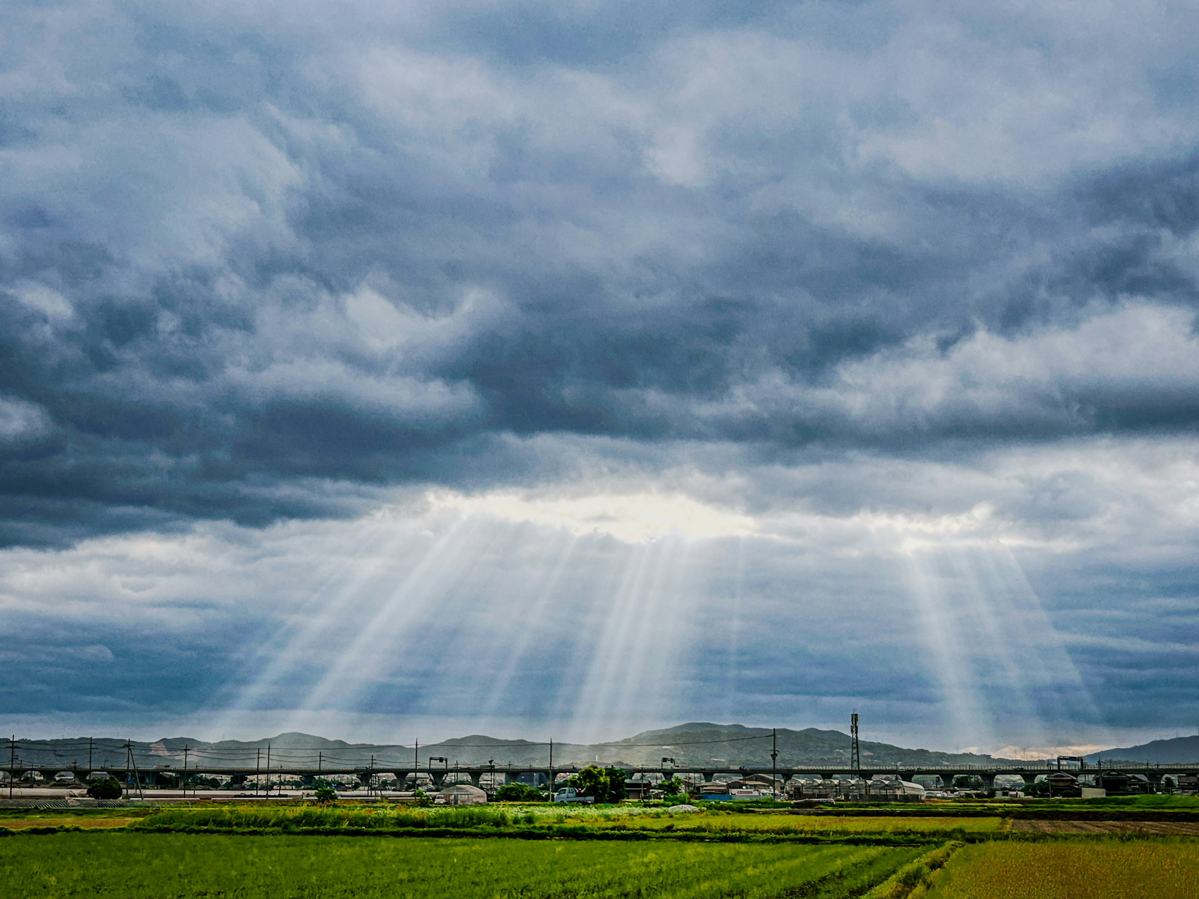 Sun rays breaking through dark clouds over a green rural landscape