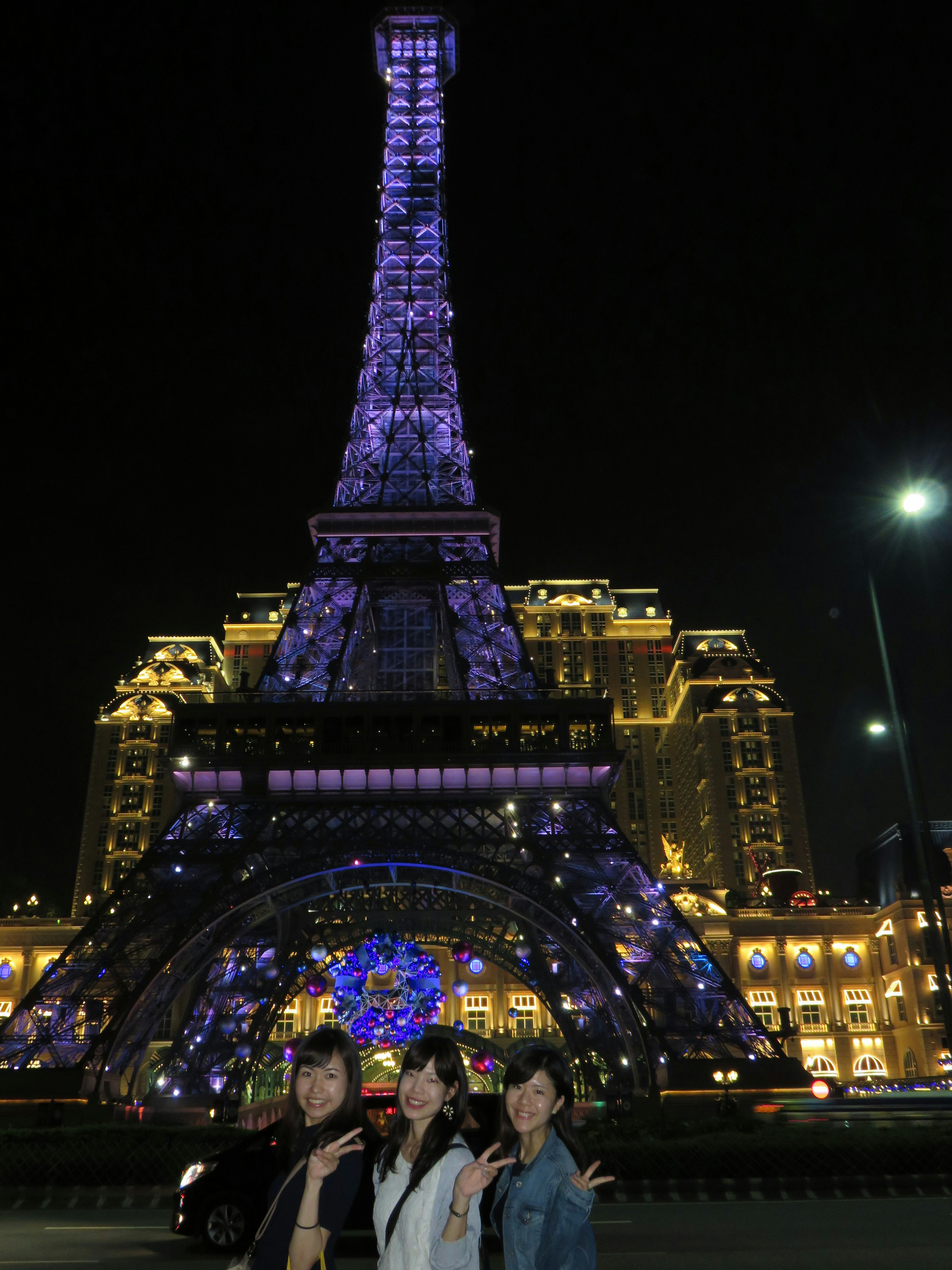 Three women posing in front of the illuminated Eiffel Tower at night