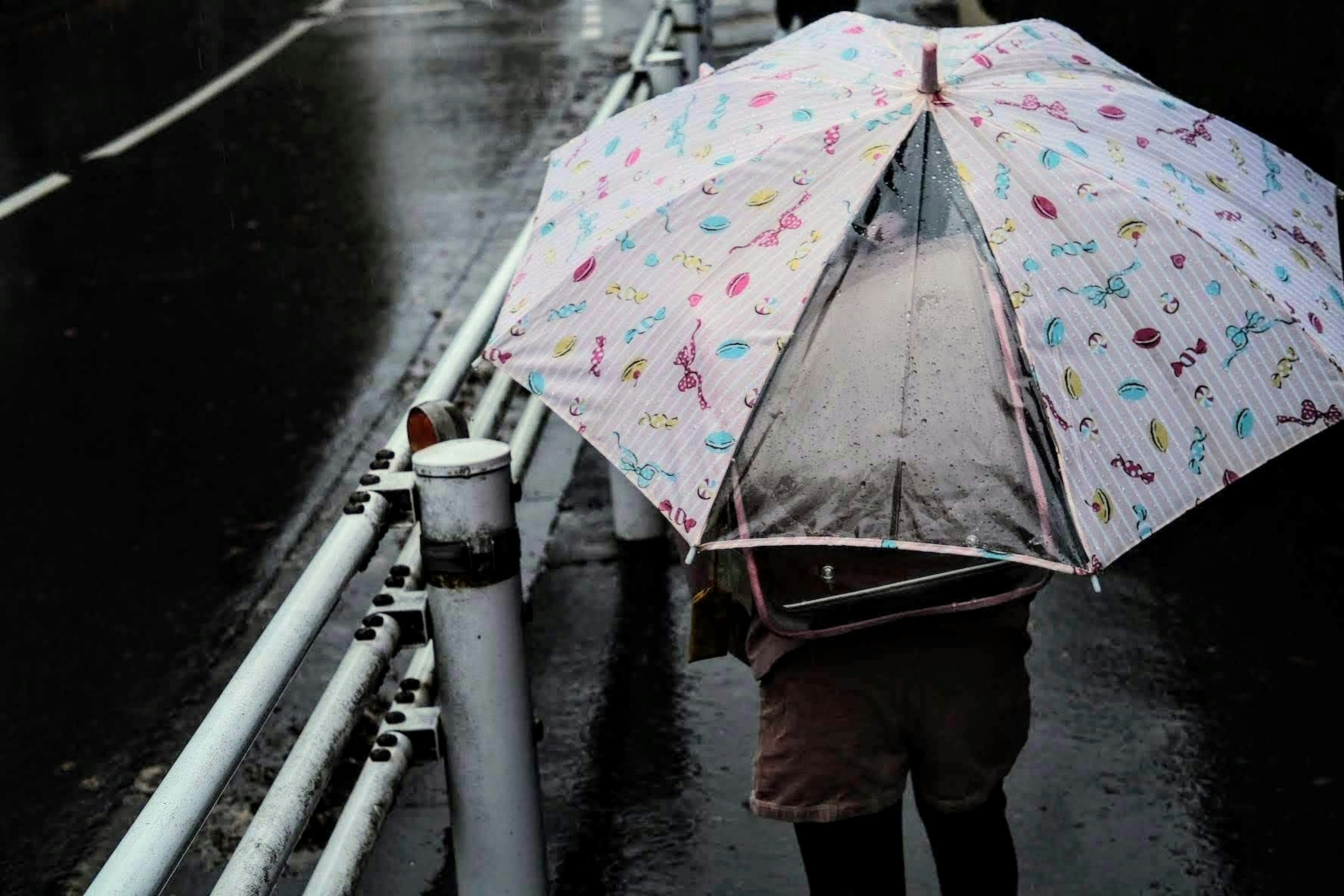 一个人在雨中走，手里拿着五颜六色的雨伞