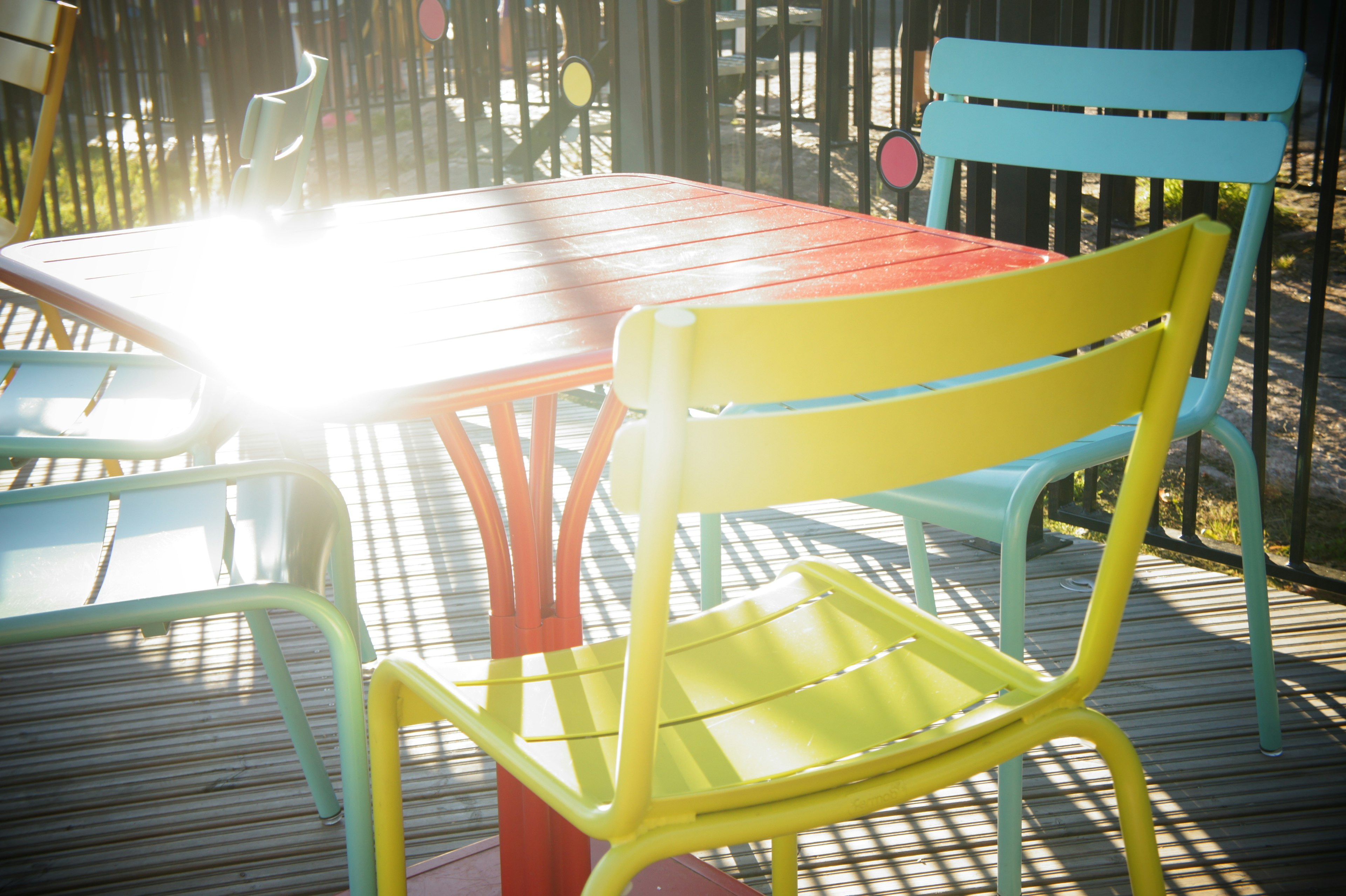 Área de comedor al aire libre colorida con mesa roja y sillas amarillas