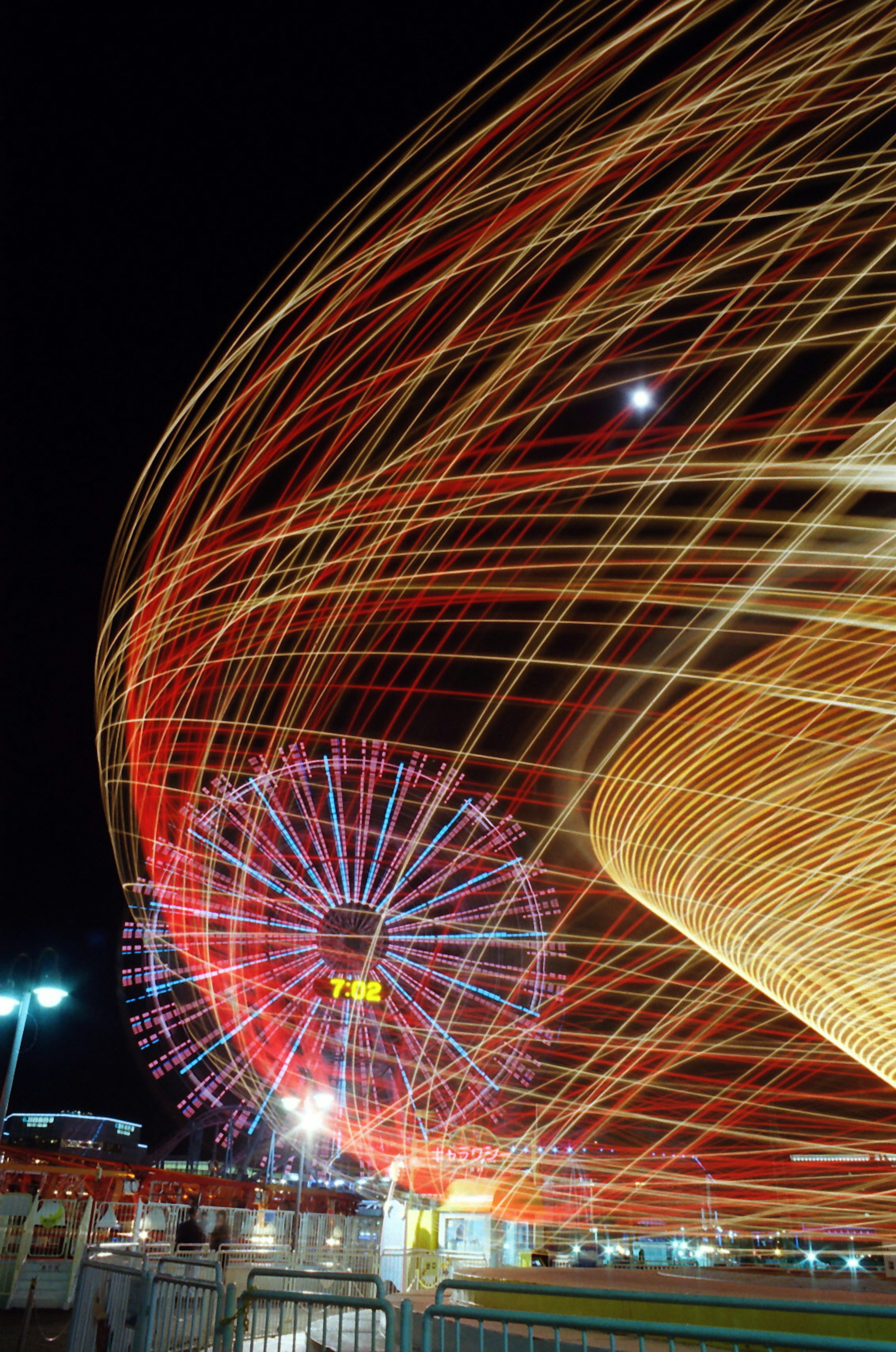 Vibrant night scene of a ferris wheel with light trails and a colorful carousel