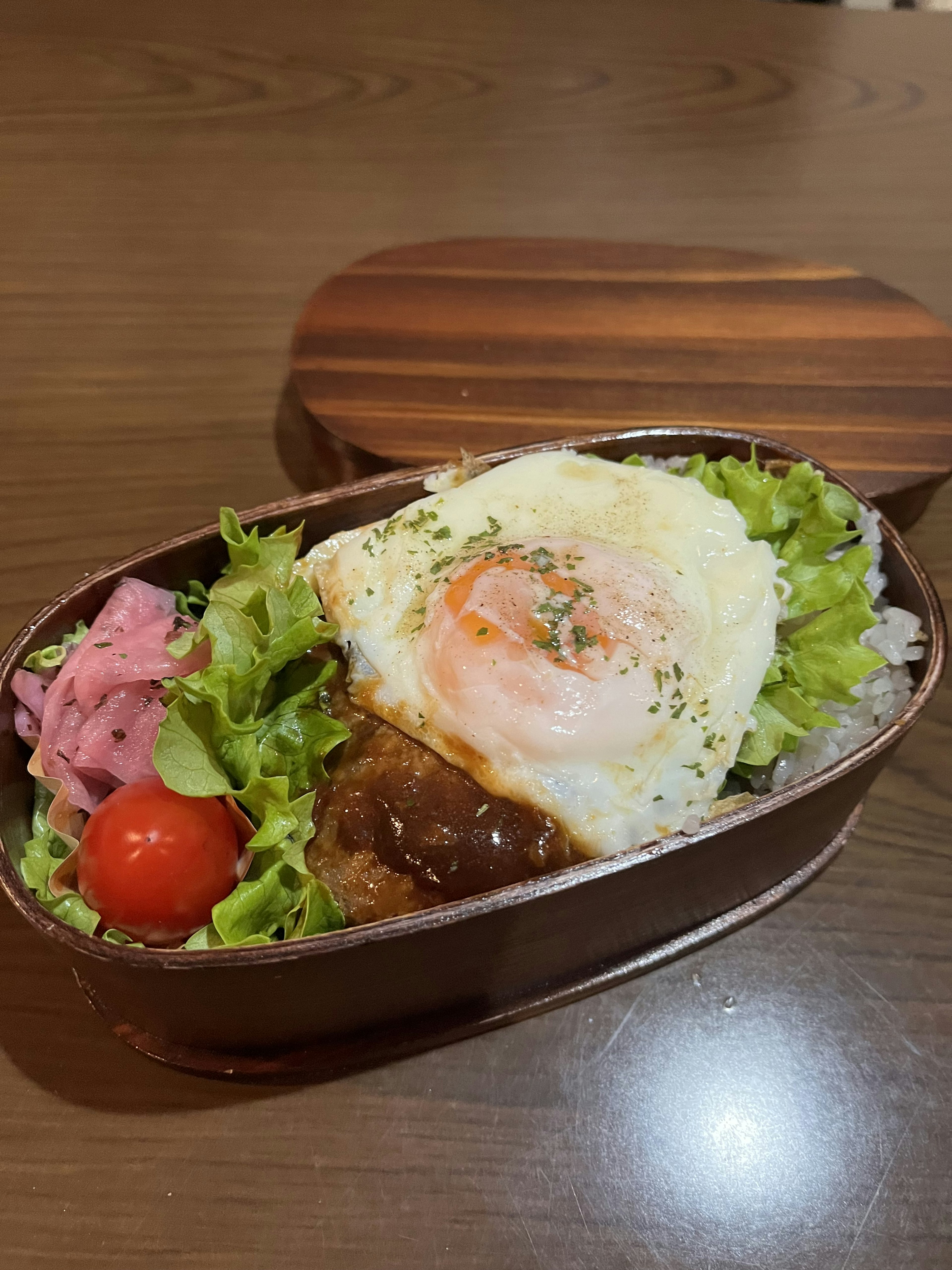 Bento-Box mit einem Spiegelei auf Reis, Salat, Kirschtomaten und Hamburger