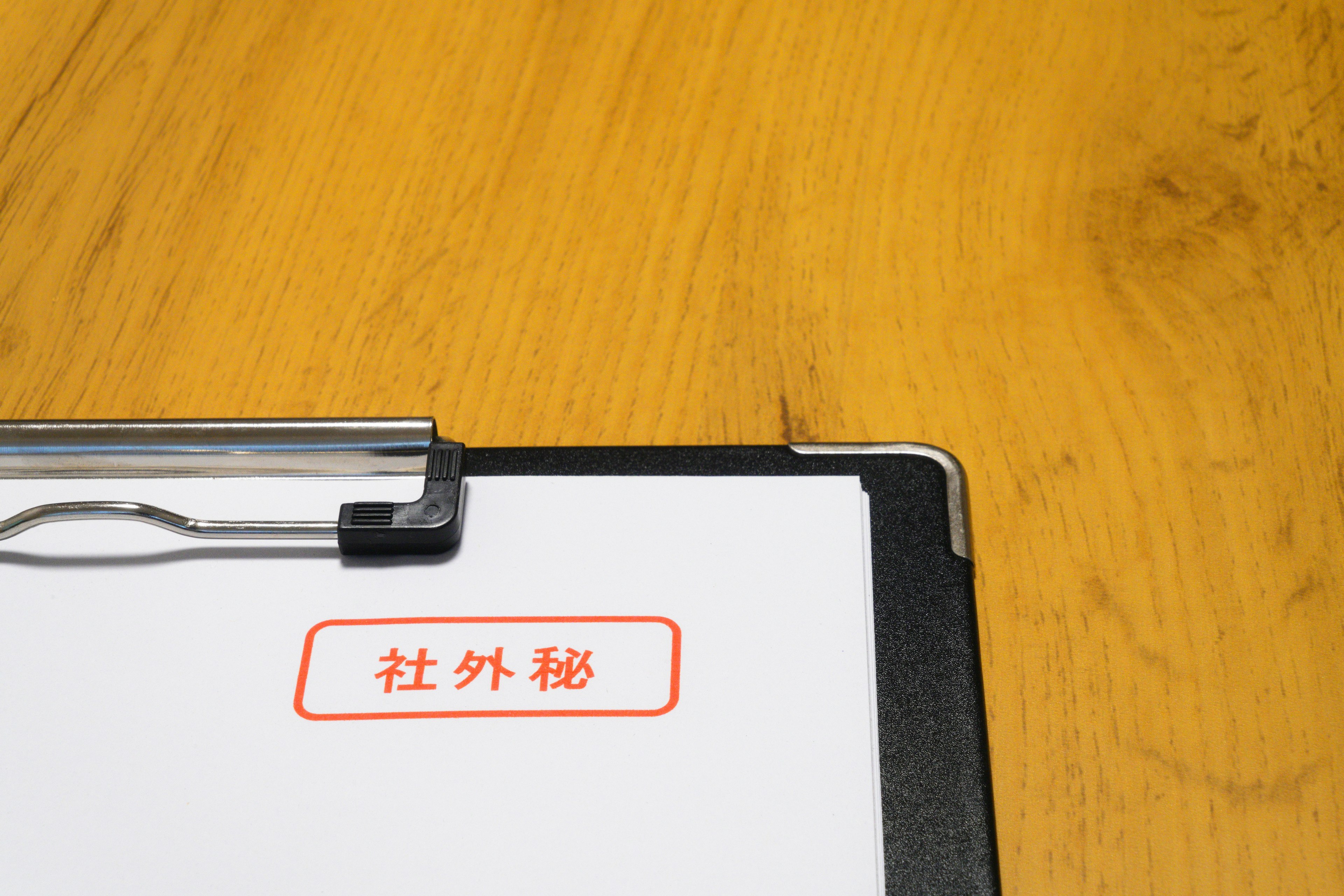 A clipboard displaying a white paper with red text on a wooden table surface