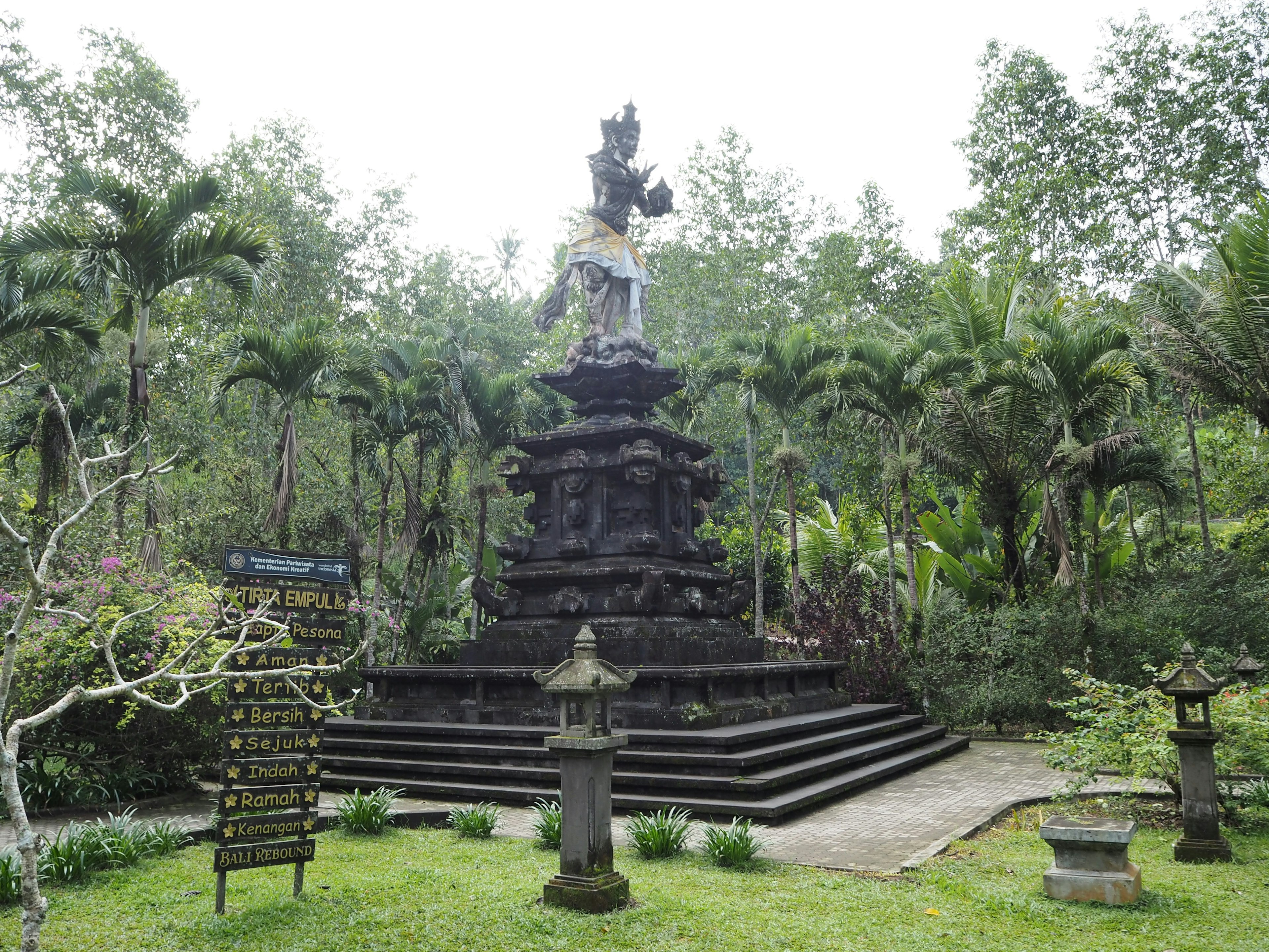 Sebuah patung batu megah dikelilingi oleh pepohonan rimbun di Bali