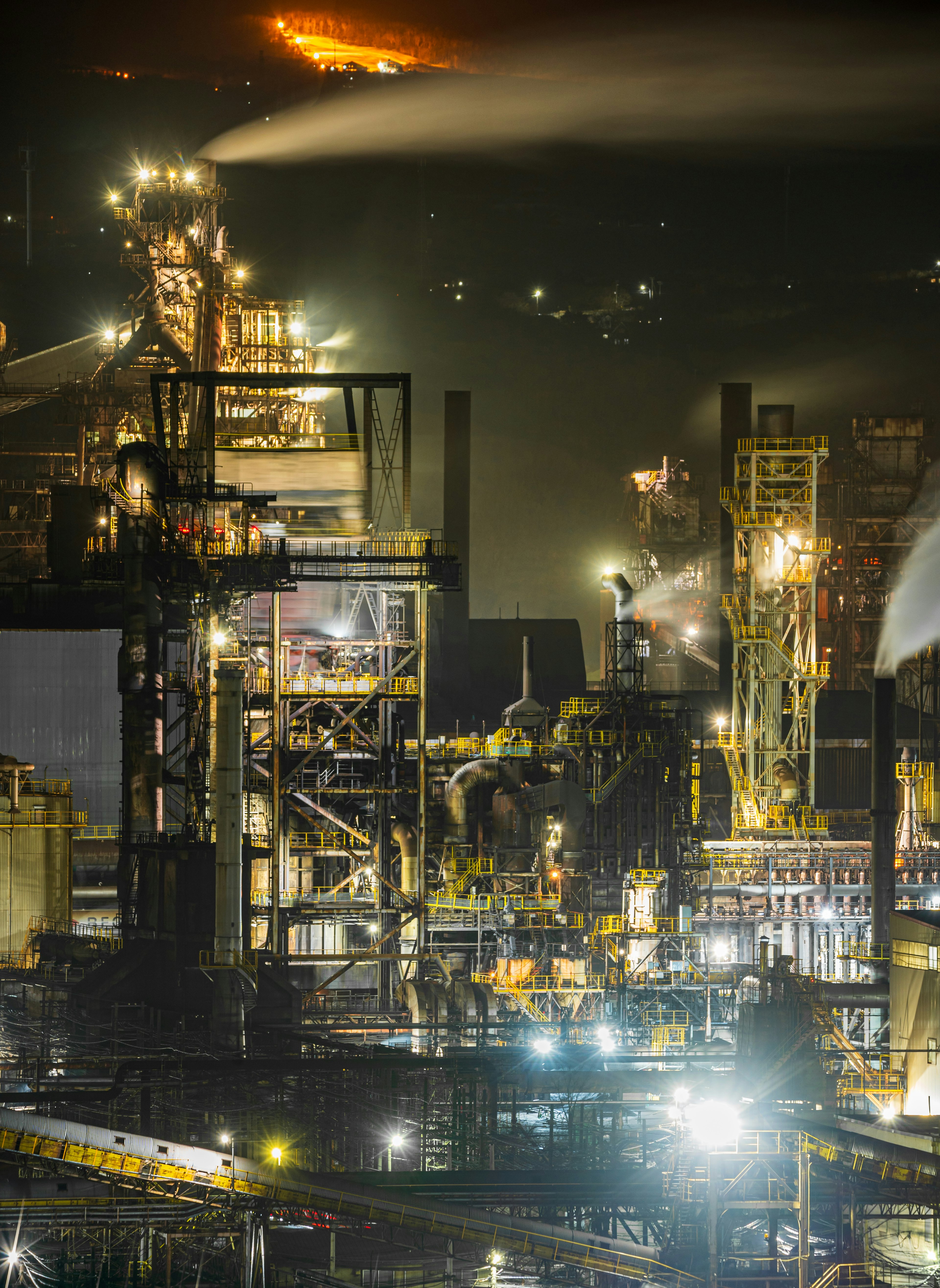 Vue nocturne d'une usine sidérurgique avec des cheminées illuminées et des structures industrielles