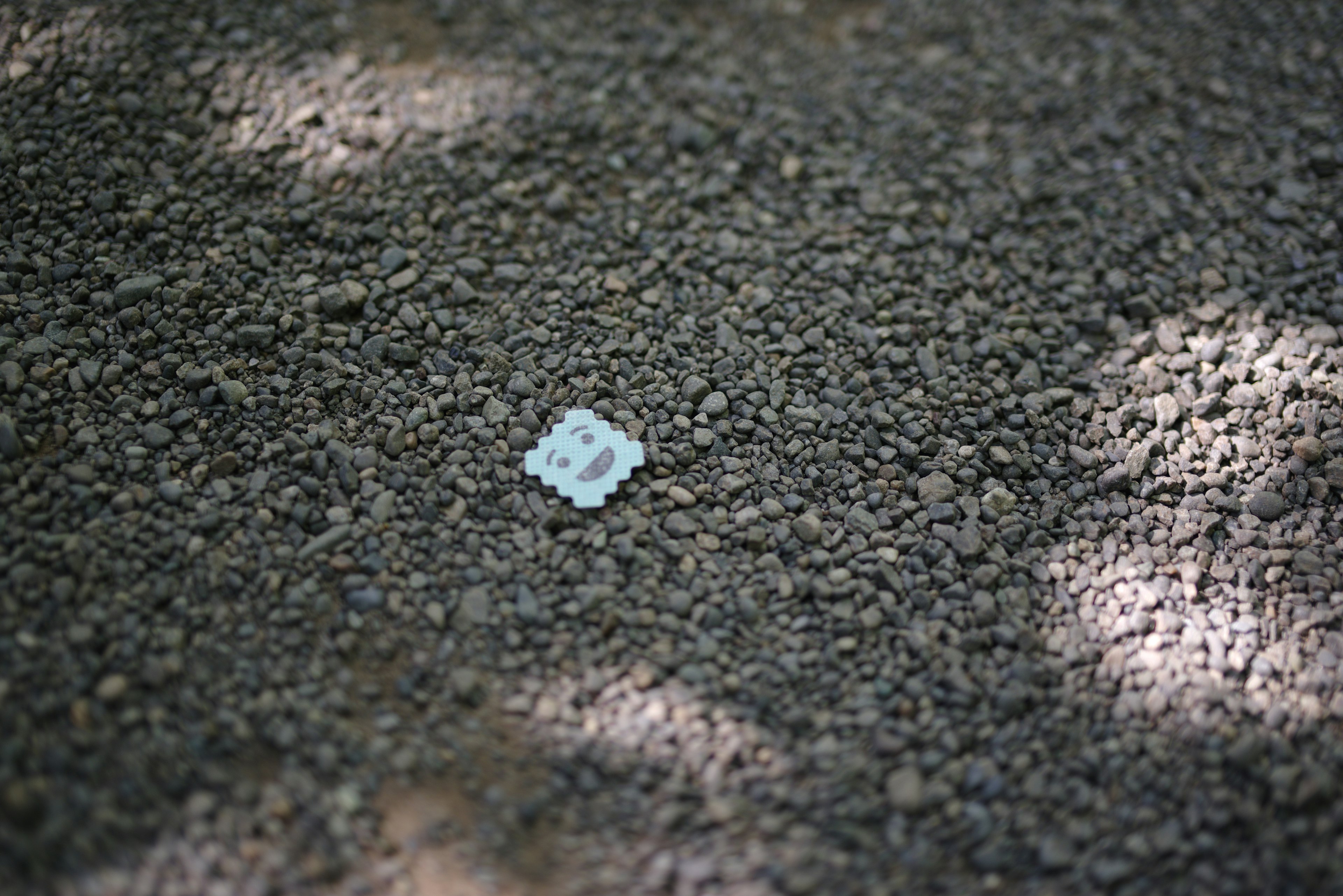 Un petit objet carré blanc posé sur un sol en gravier