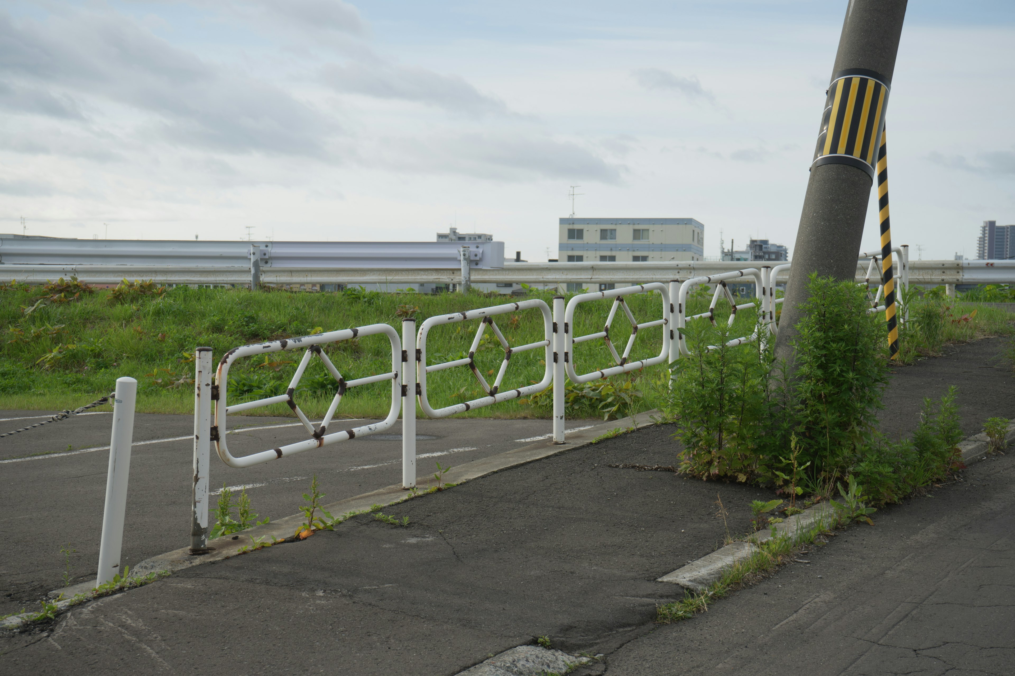 White fence beside a road with grass and a yellow and black striped pole