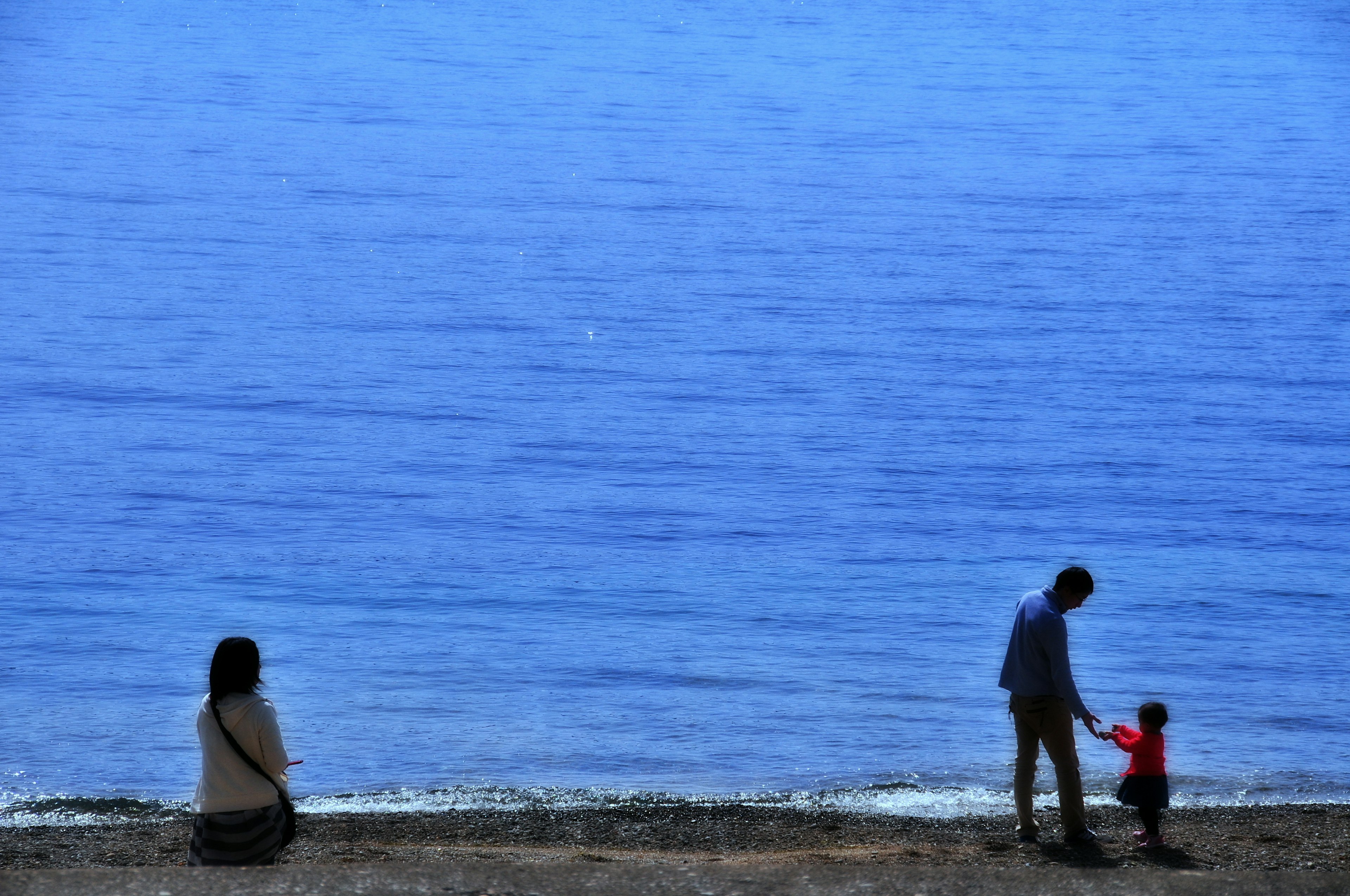 ครอบครัวเดินเล่นริมชายหาดที่มีทะเลสีน้ำเงินอยู่ด้านหลัง