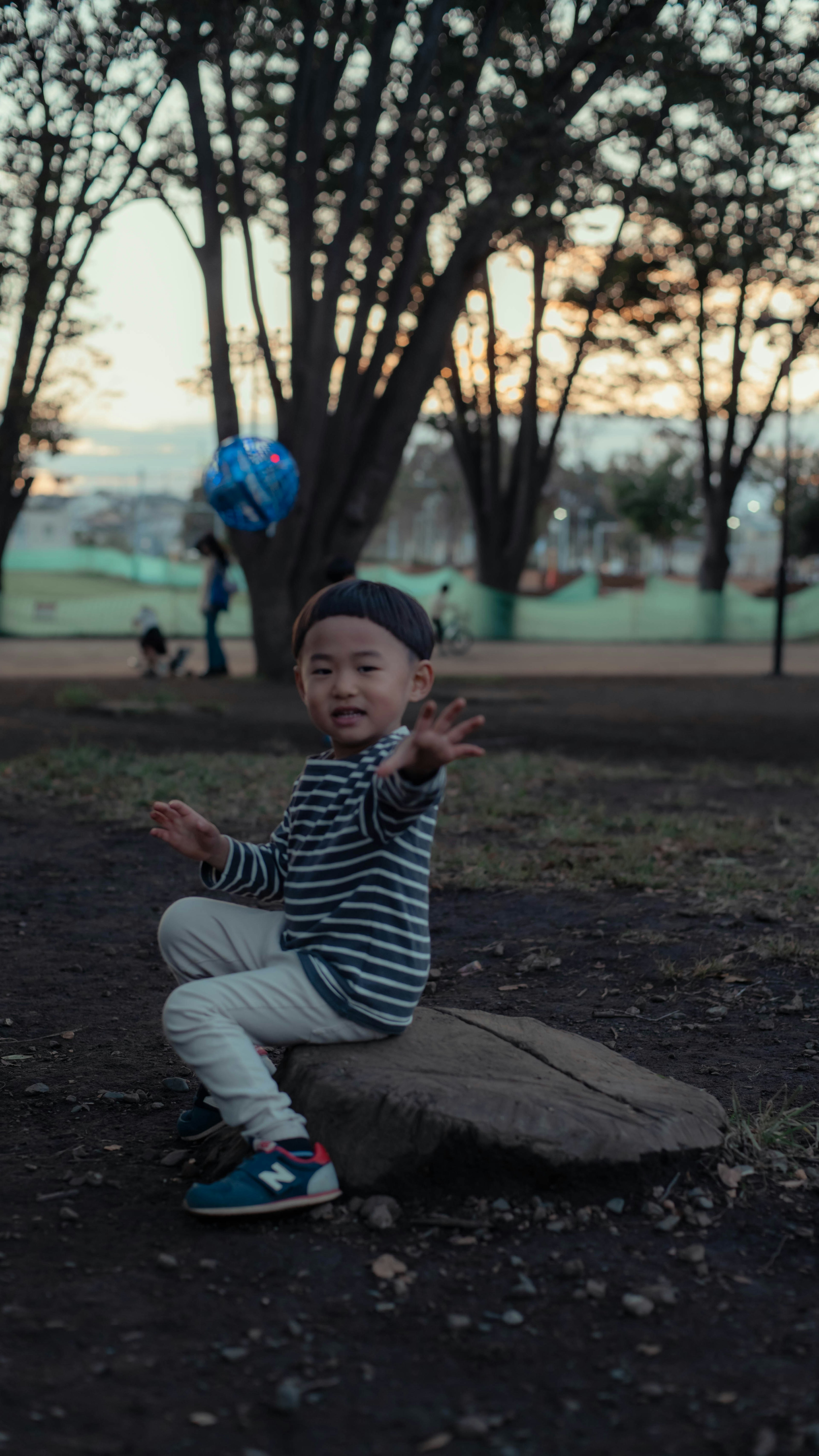 Child sitting on a rock in a park holding a blue balloon