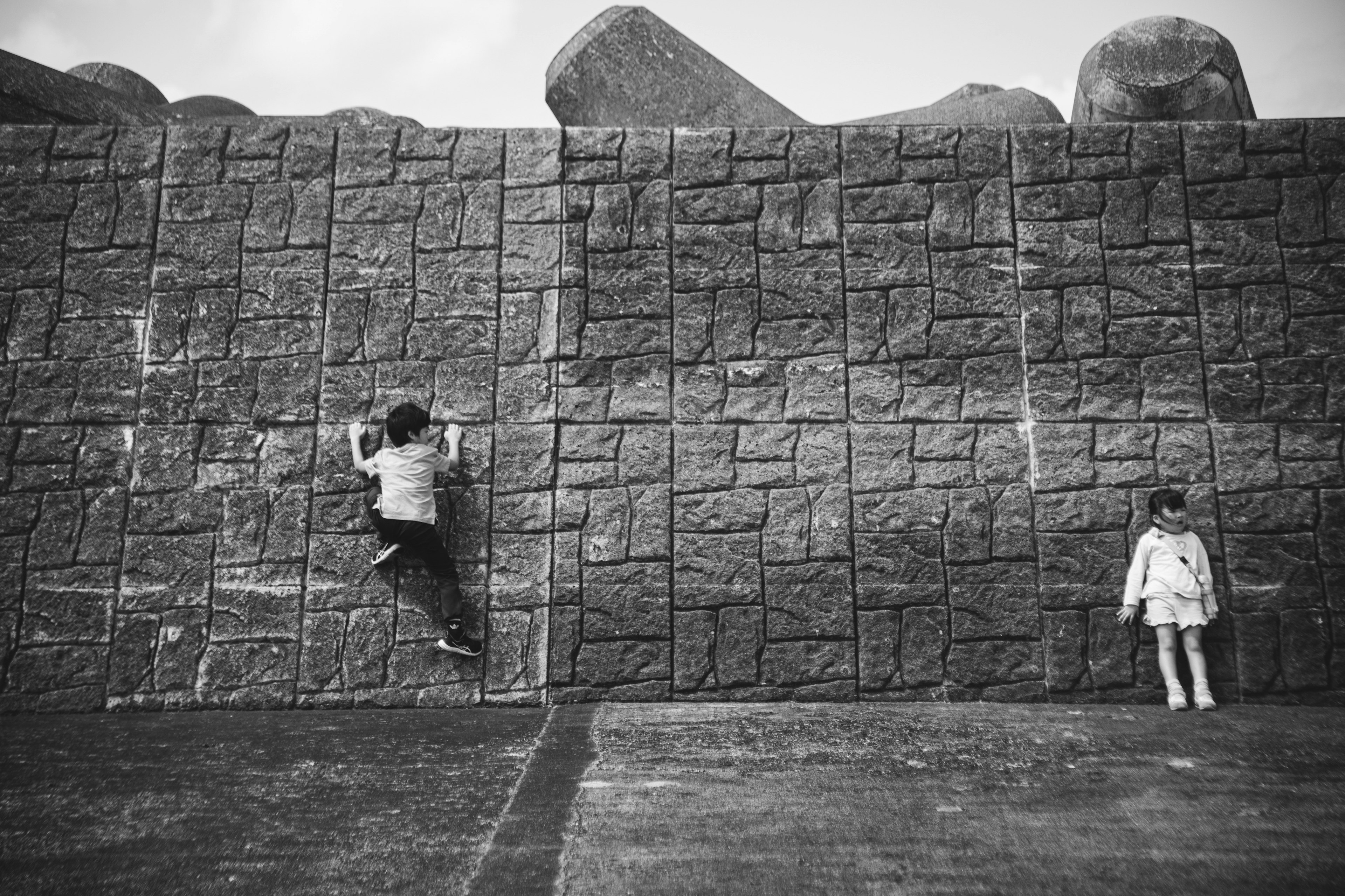 A child climbing a textured wall with a girl standing nearby