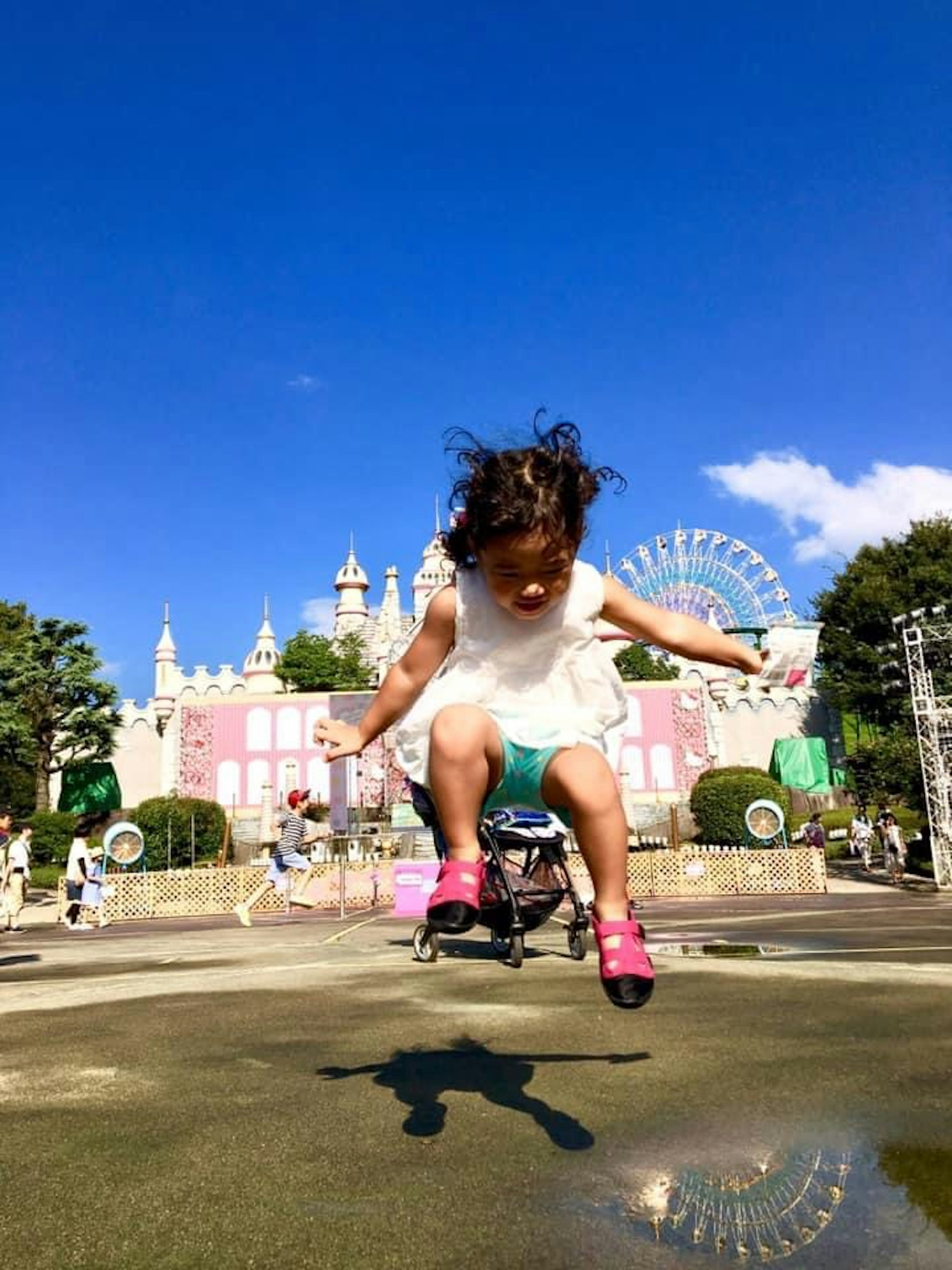 Niña con un vestido blanco saltando alegremente con atracciones de parque de diversiones al fondo