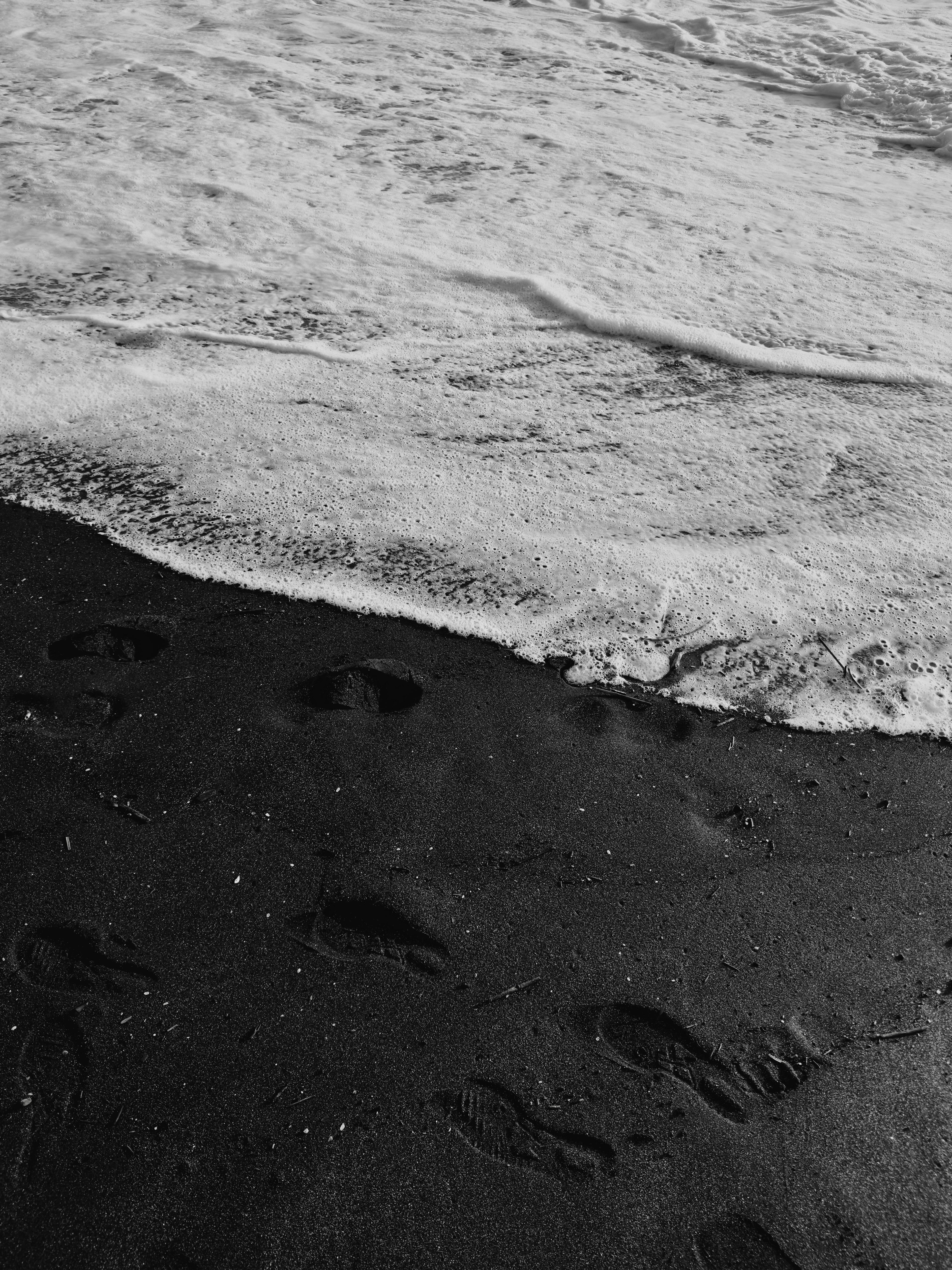 Fußabdrücke am schwarzen Sandstrand mit heranrollenden Wellen