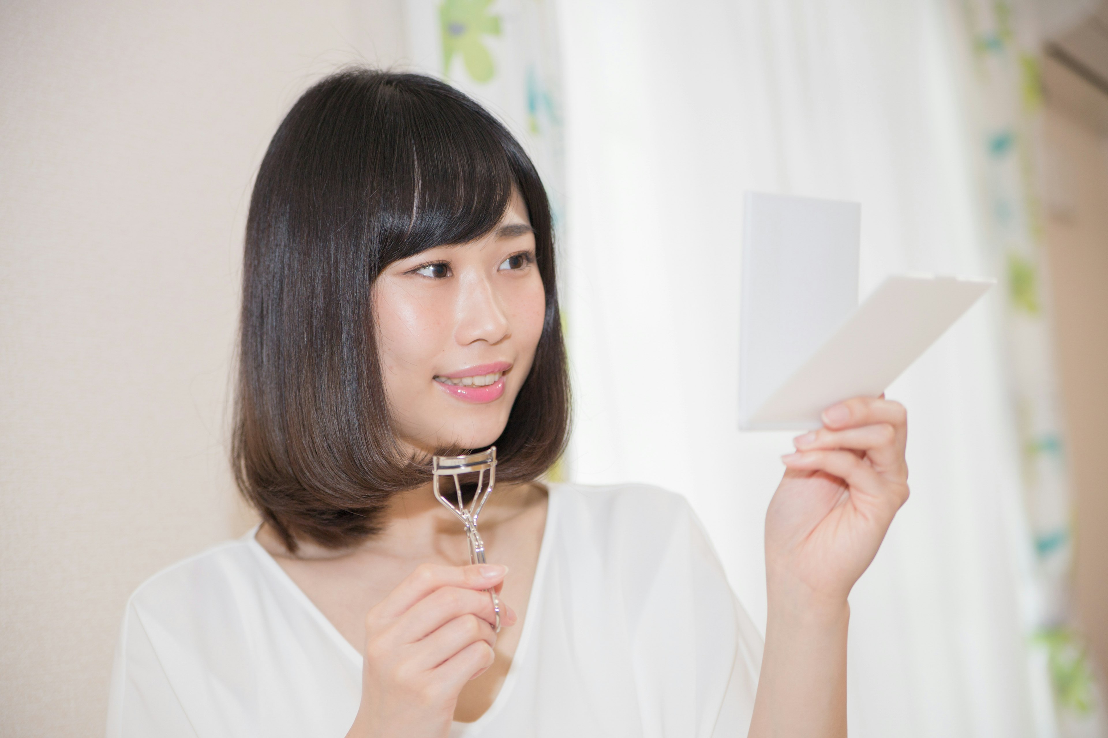 Woman holding eyelash curler while looking at a note