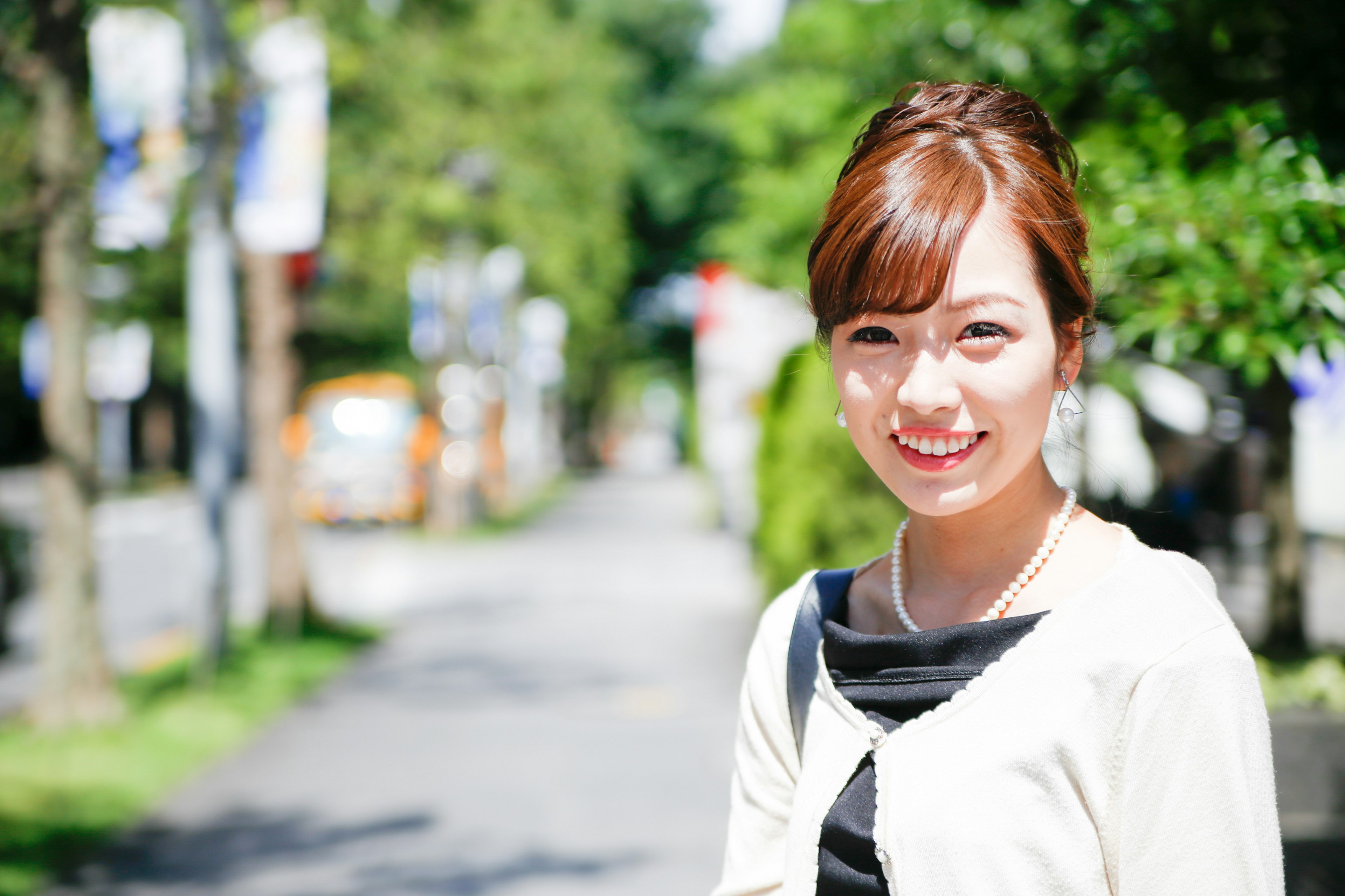 A smiling woman standing on a sidewalk in bright sunlight