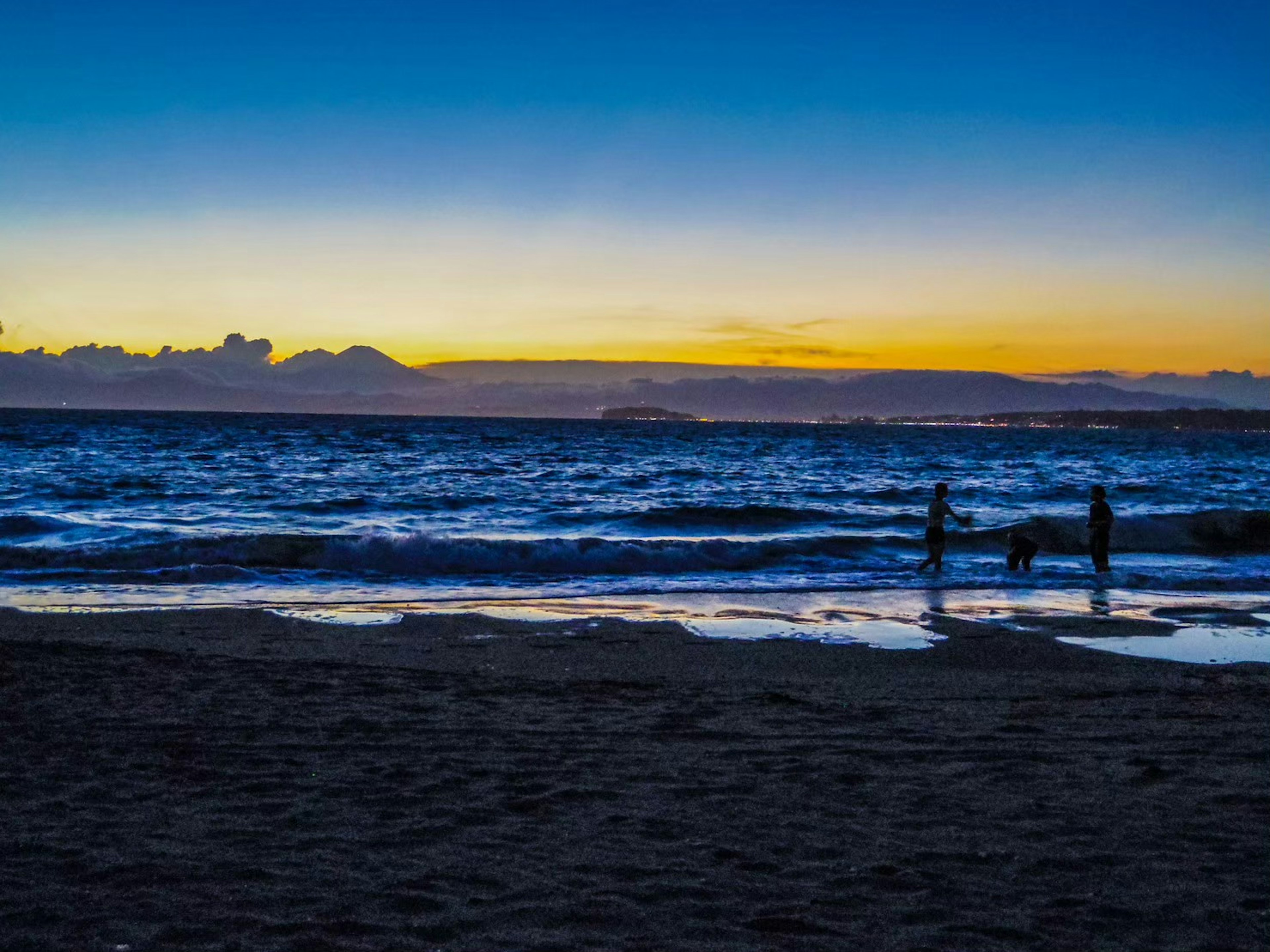 Silhouetten von Menschen und einem Hund am Strand bei Sonnenuntergang