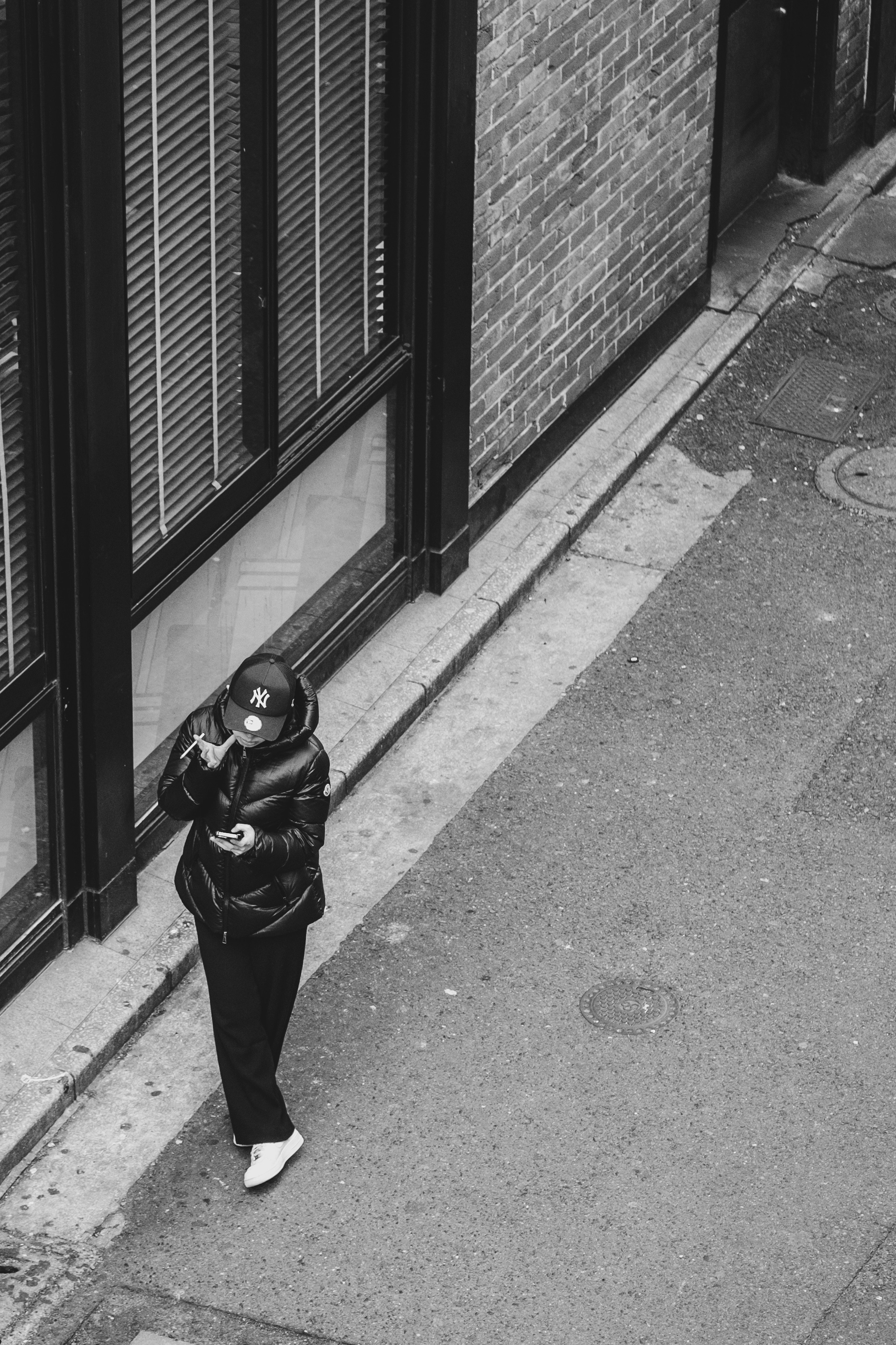 A person in black clothing checking their smartphone in a narrow alleyway monochrome image