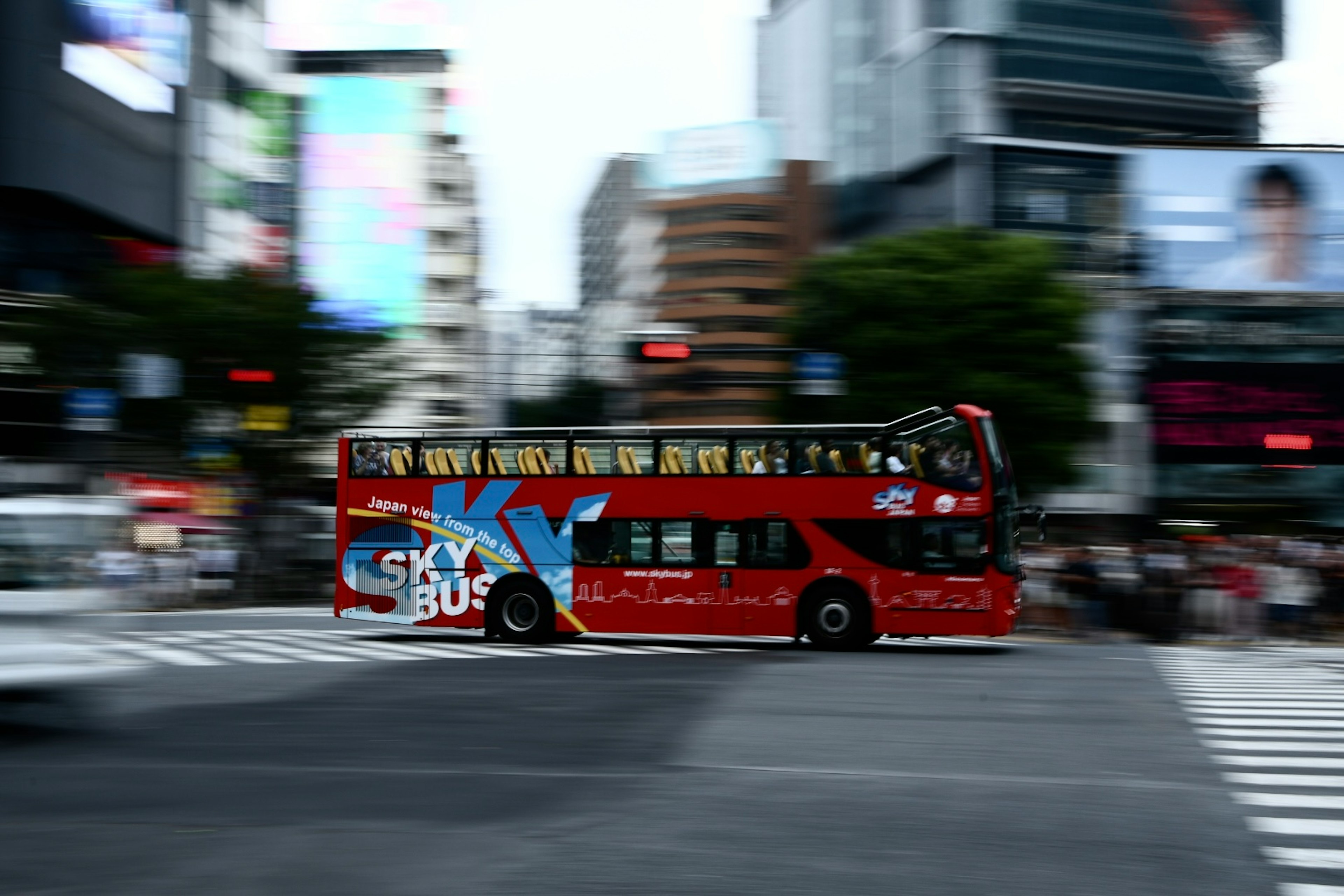 赤い観光バスが繁華街を走る写真