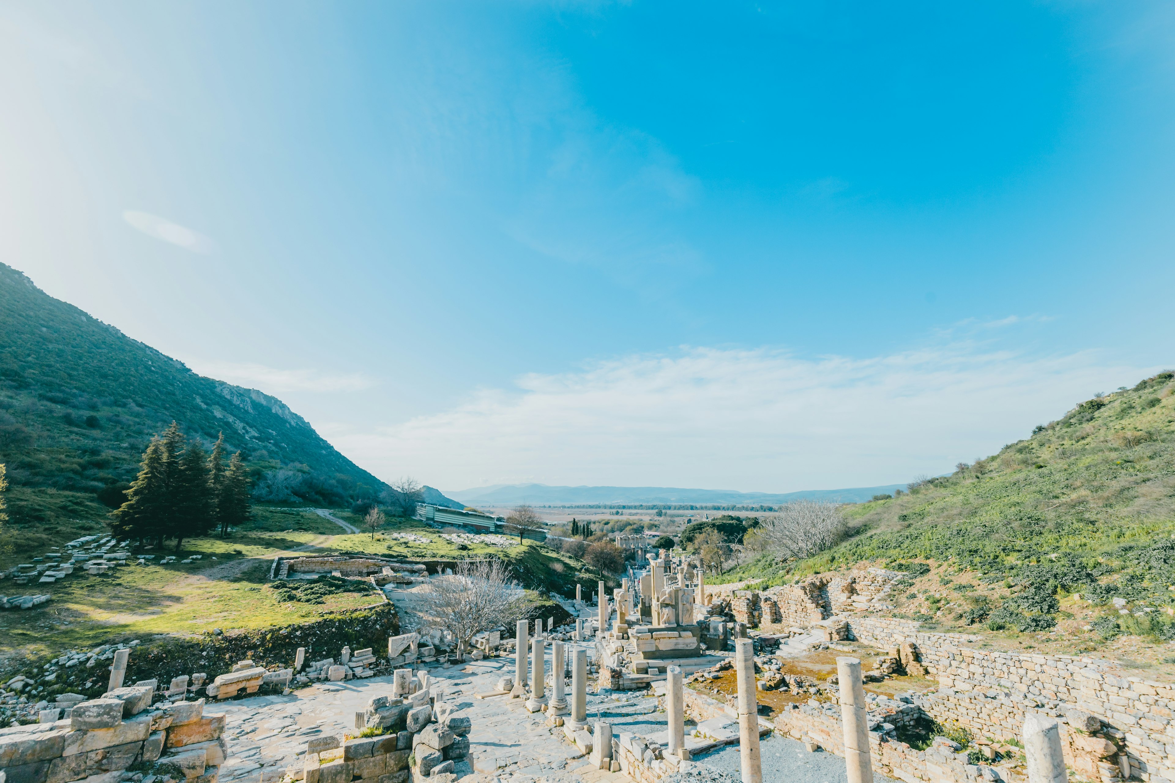 Vista panorámica de ruinas antiguas con columnas bajo un cielo azul y colinas verdes