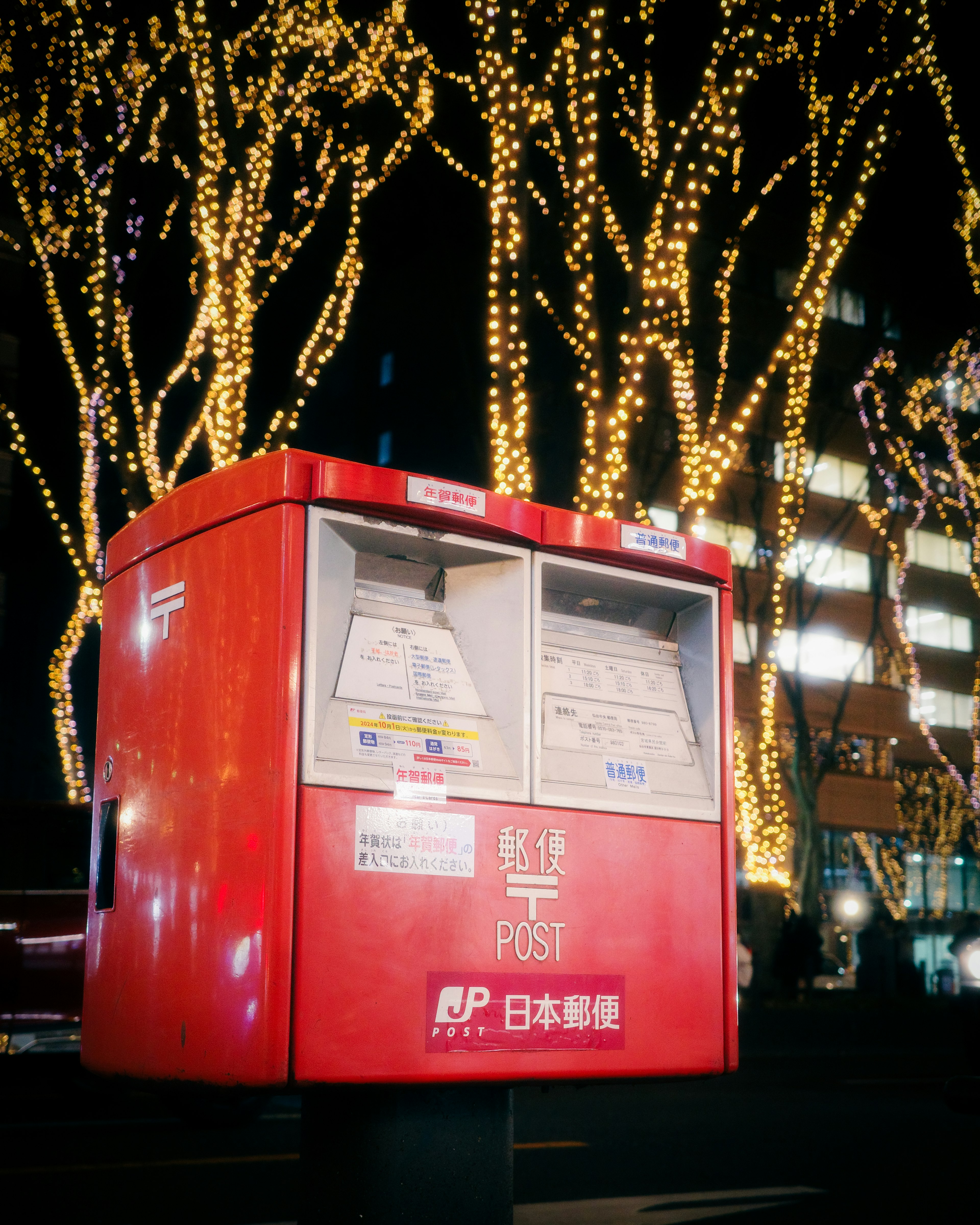 Buzón rojo iluminado por las luces de la ciudad de noche