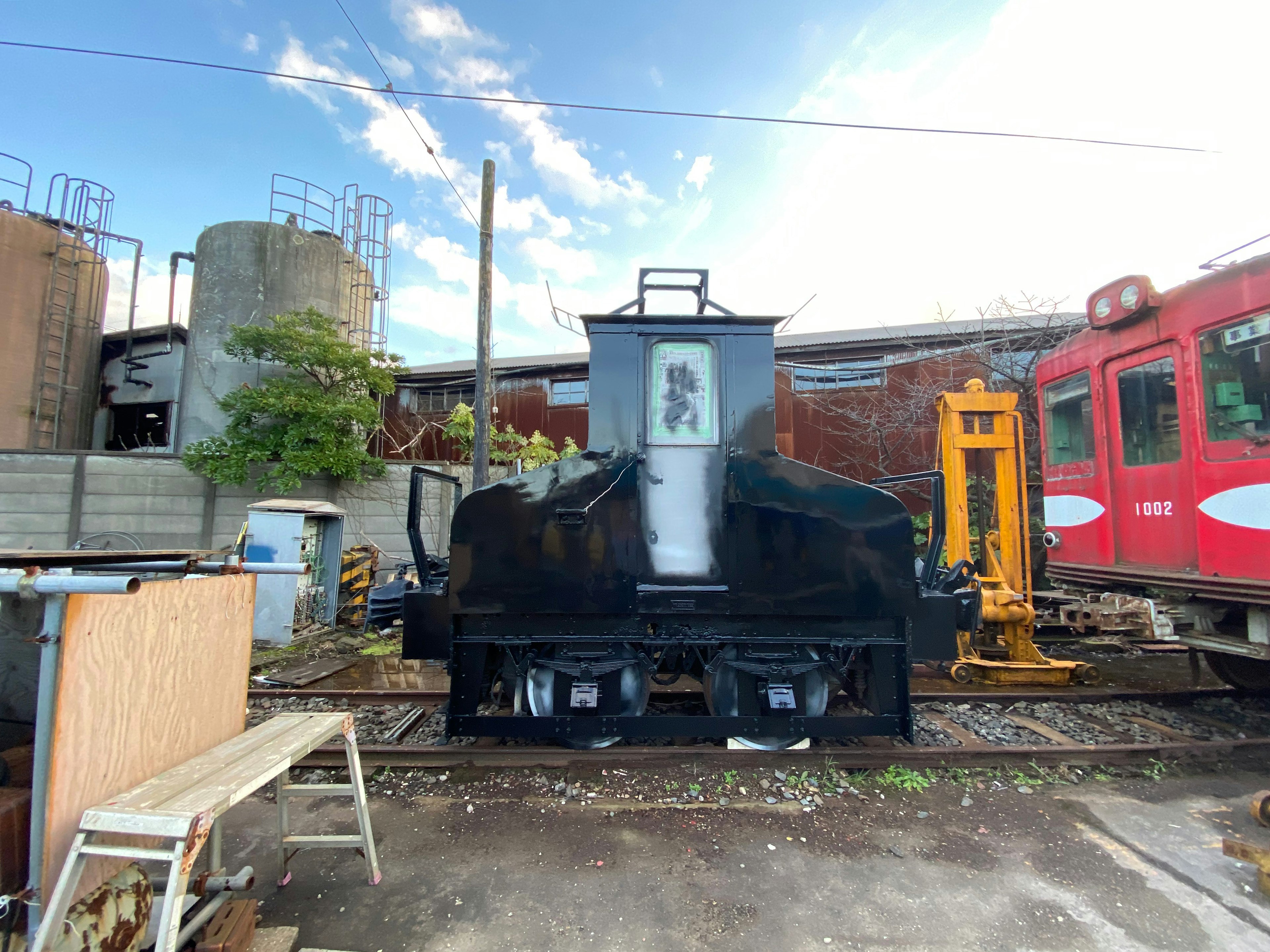 Locomotora negra sobre las vías con fondo industrial y cielo azul