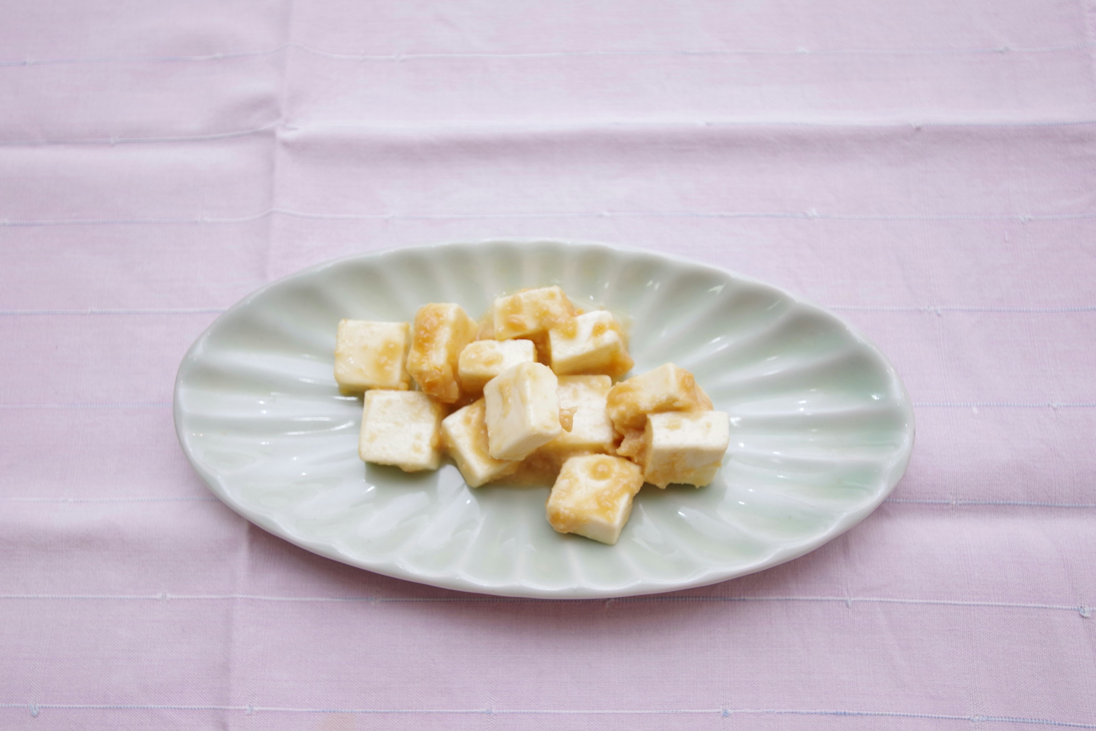 Cubos de tofu blanco dispuestos en un plato verde claro