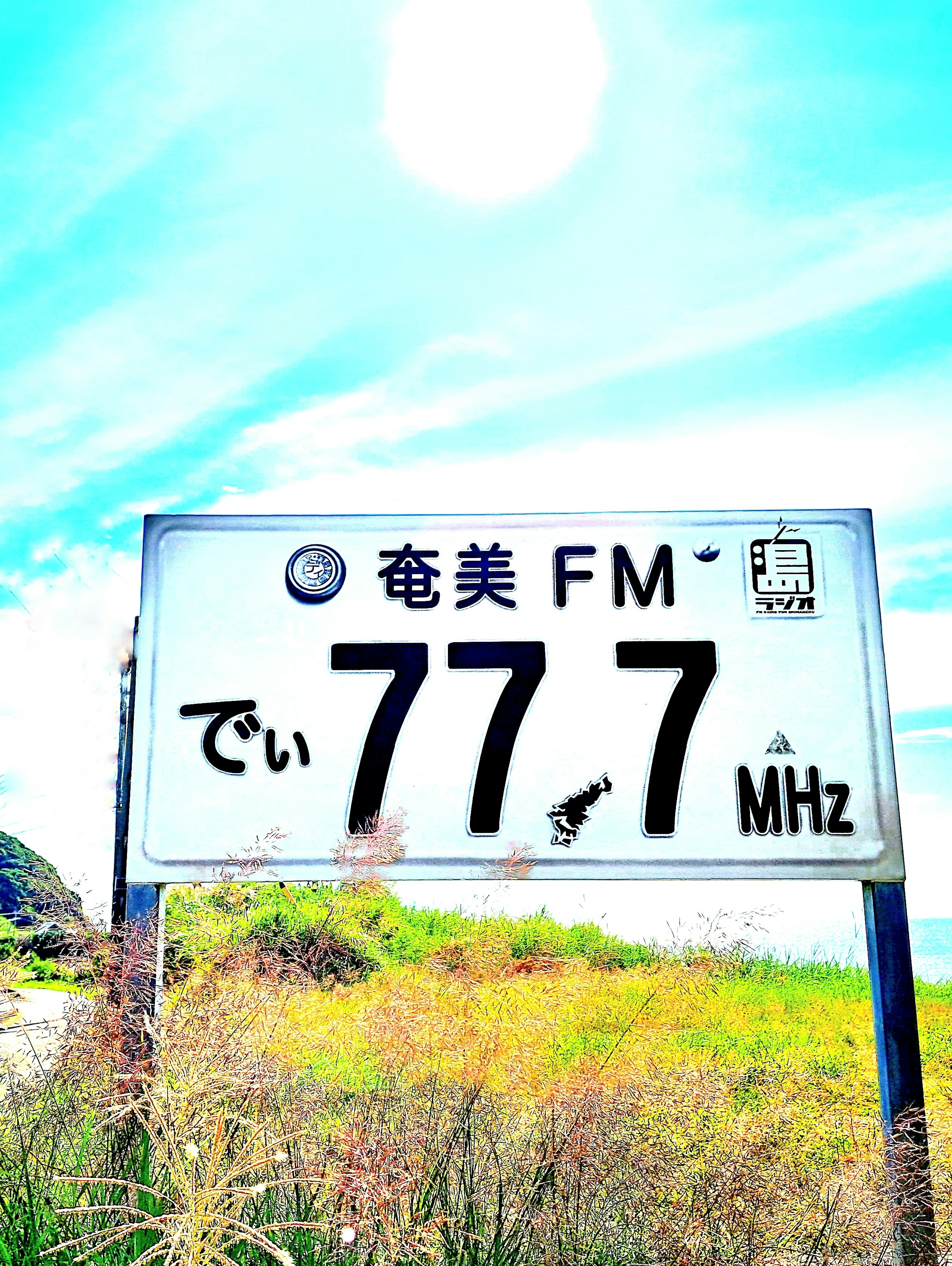 青空の下にあるラジオ局の看板 FM で 77.7 MHz と表示されている