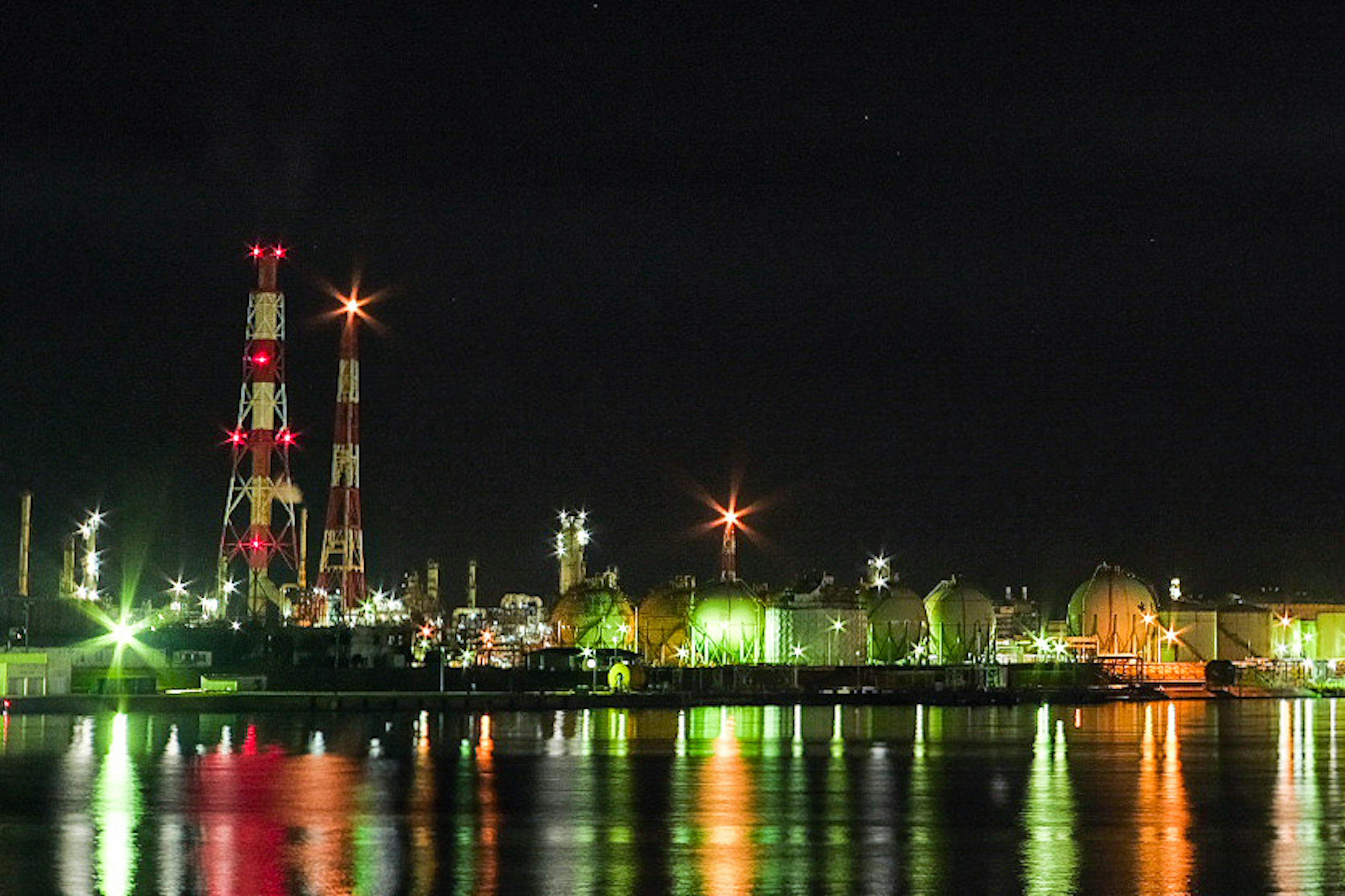 Night view of a factory with colorful lights reflecting on the water