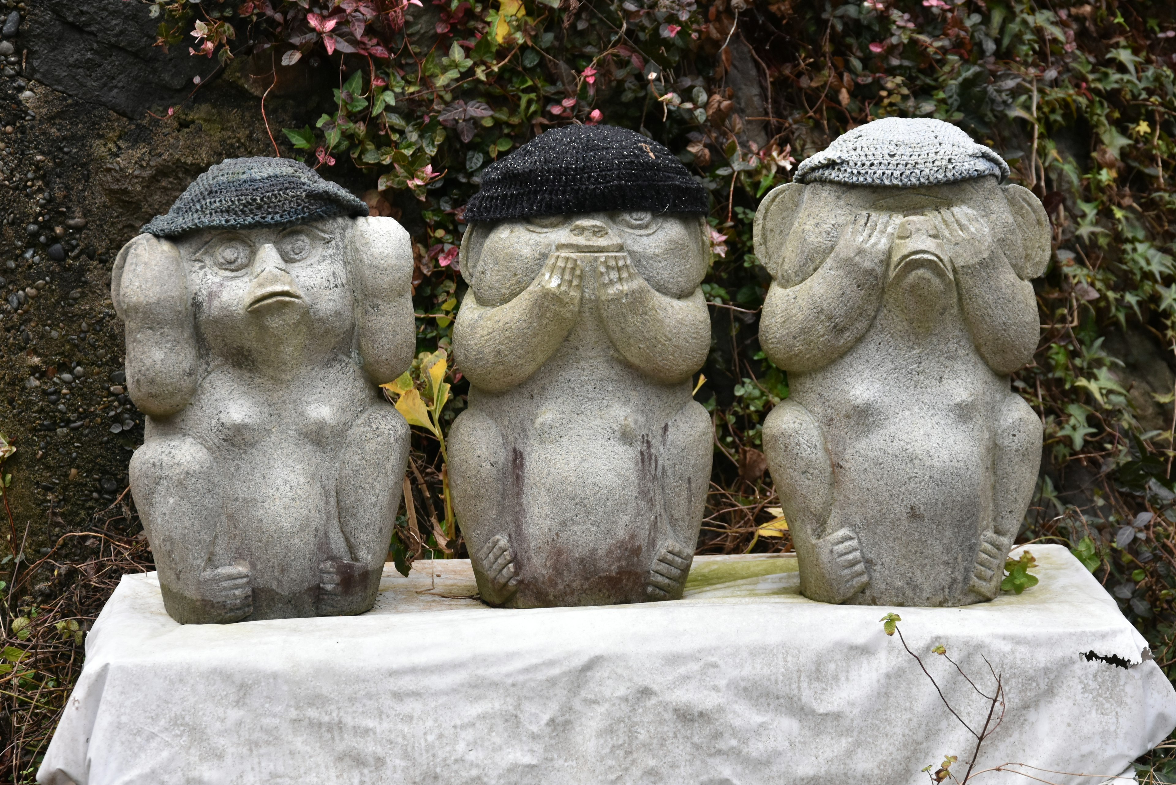 Three stone statues wearing hats standing side by side