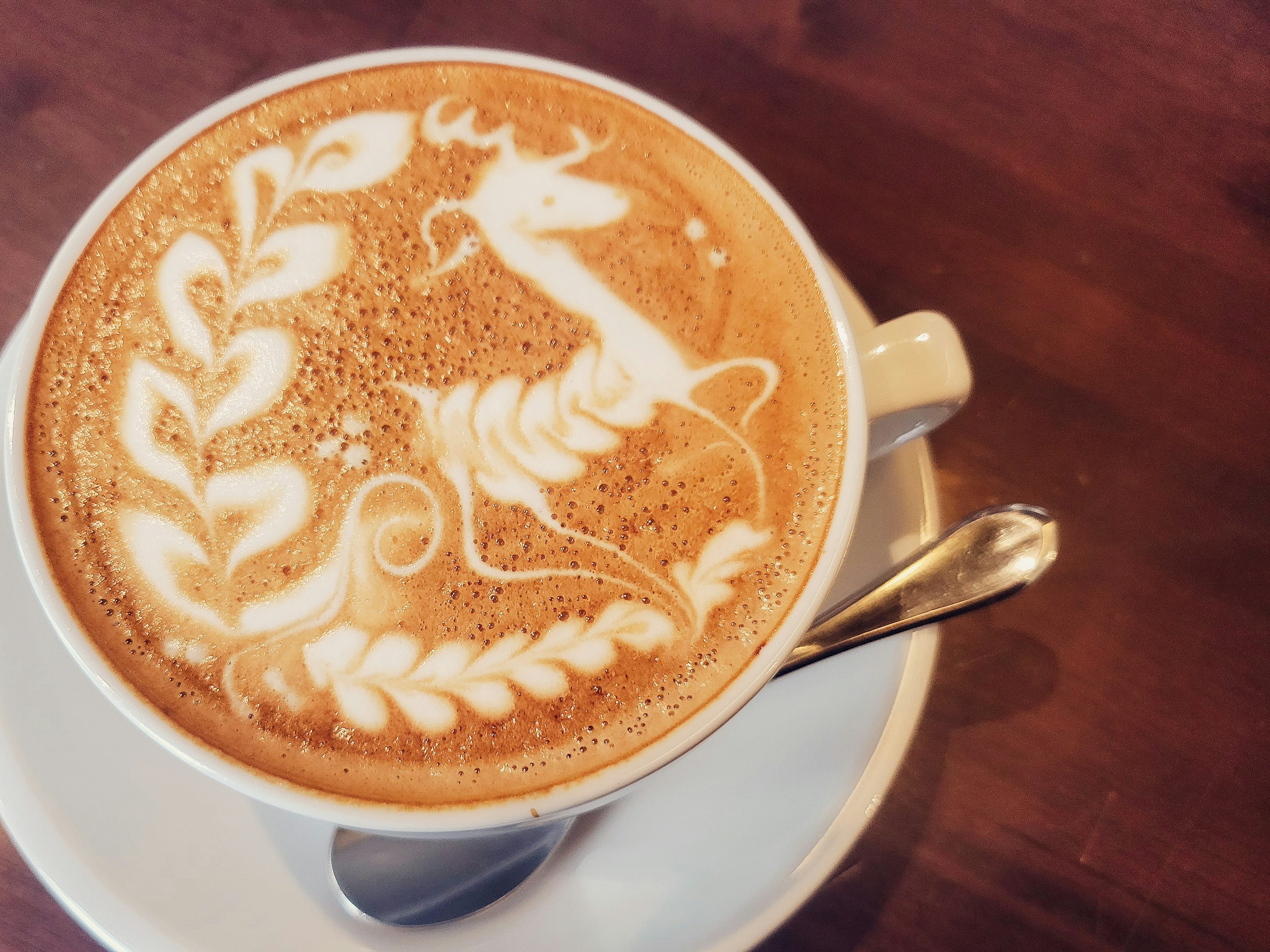 Latte art featuring a deer and leaf patterns in a coffee cup