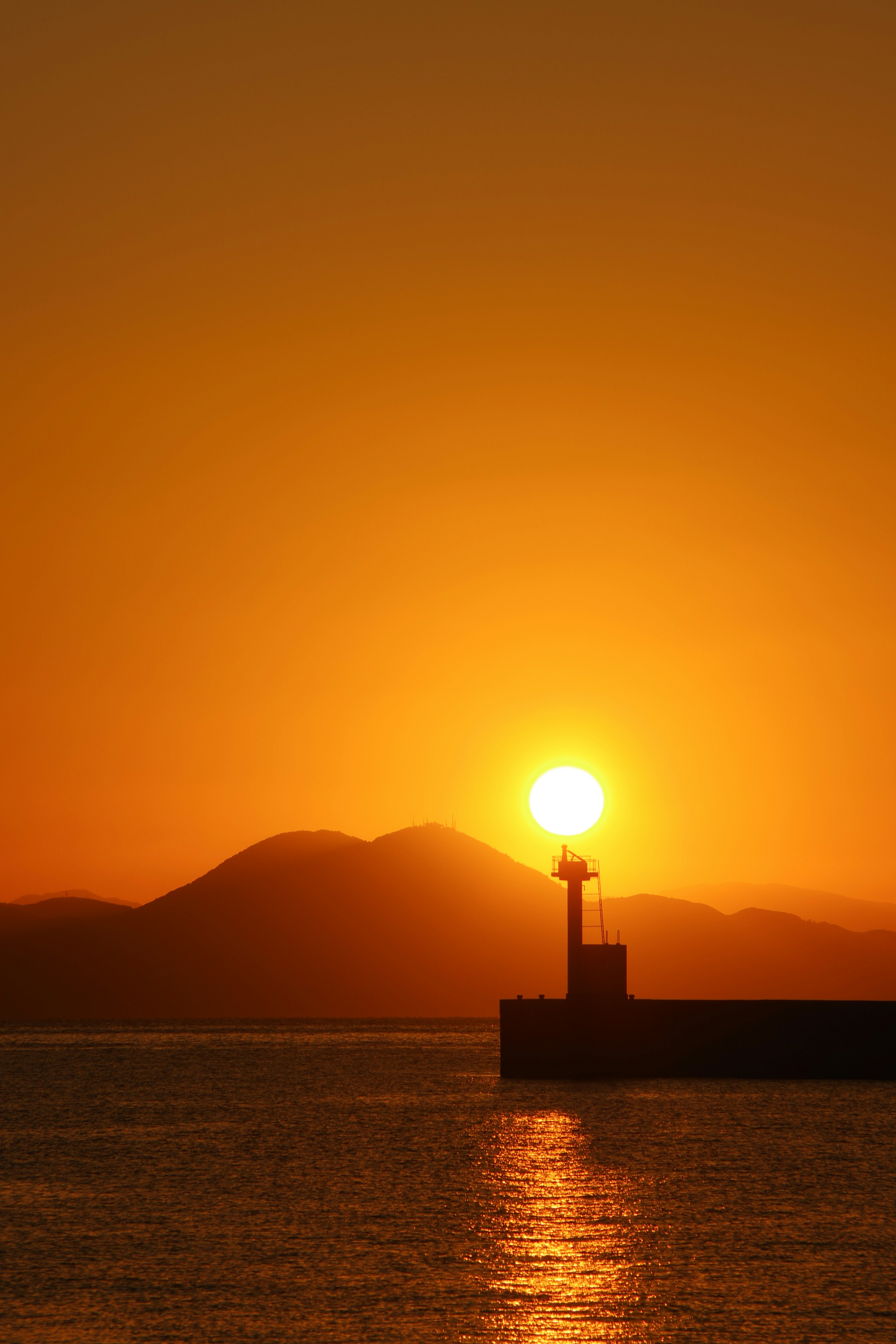 Beautiful landscape of sunset over mountains lighthouse silhouetted against the sun