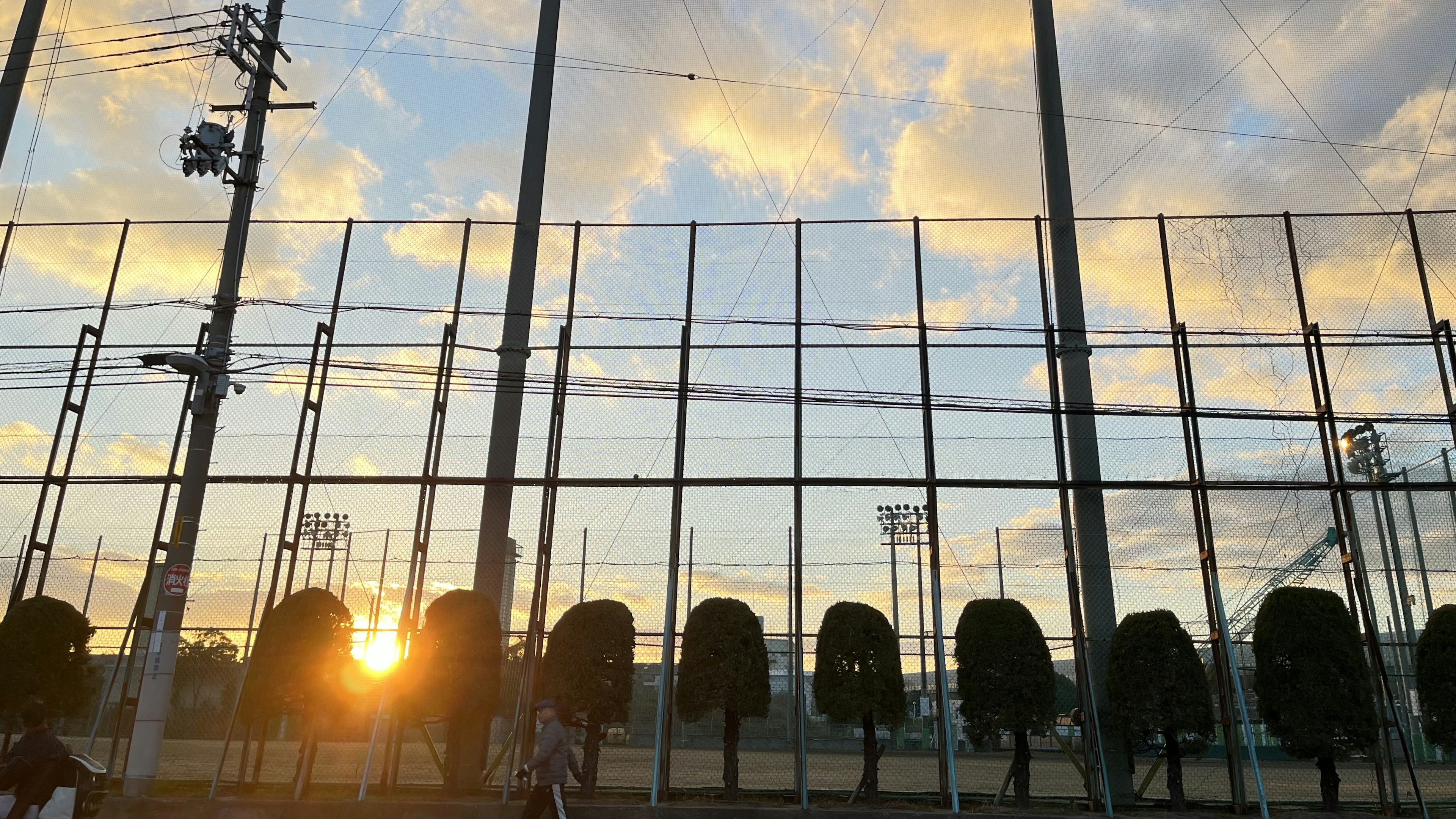 夕日が見えるスポーツフィールドのネット越しの風景