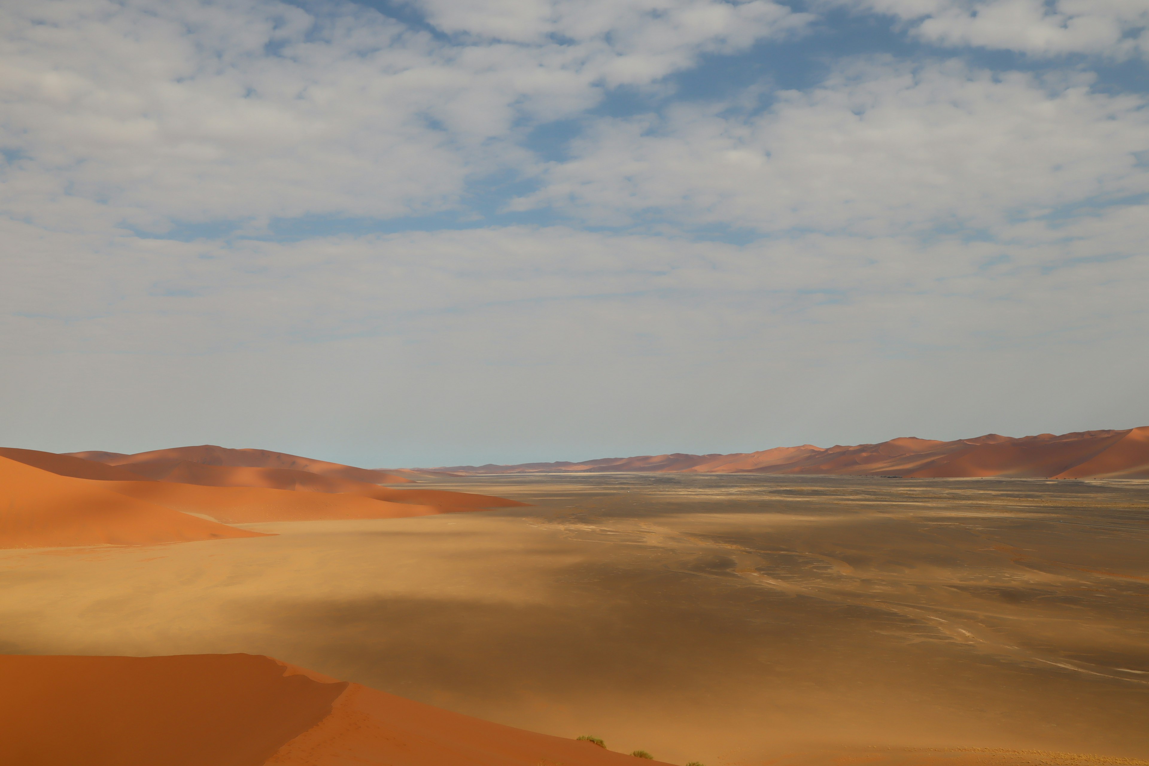 Weite Wüstenlandschaft mit orangefarbenen Sanddünen und blauem Himmel