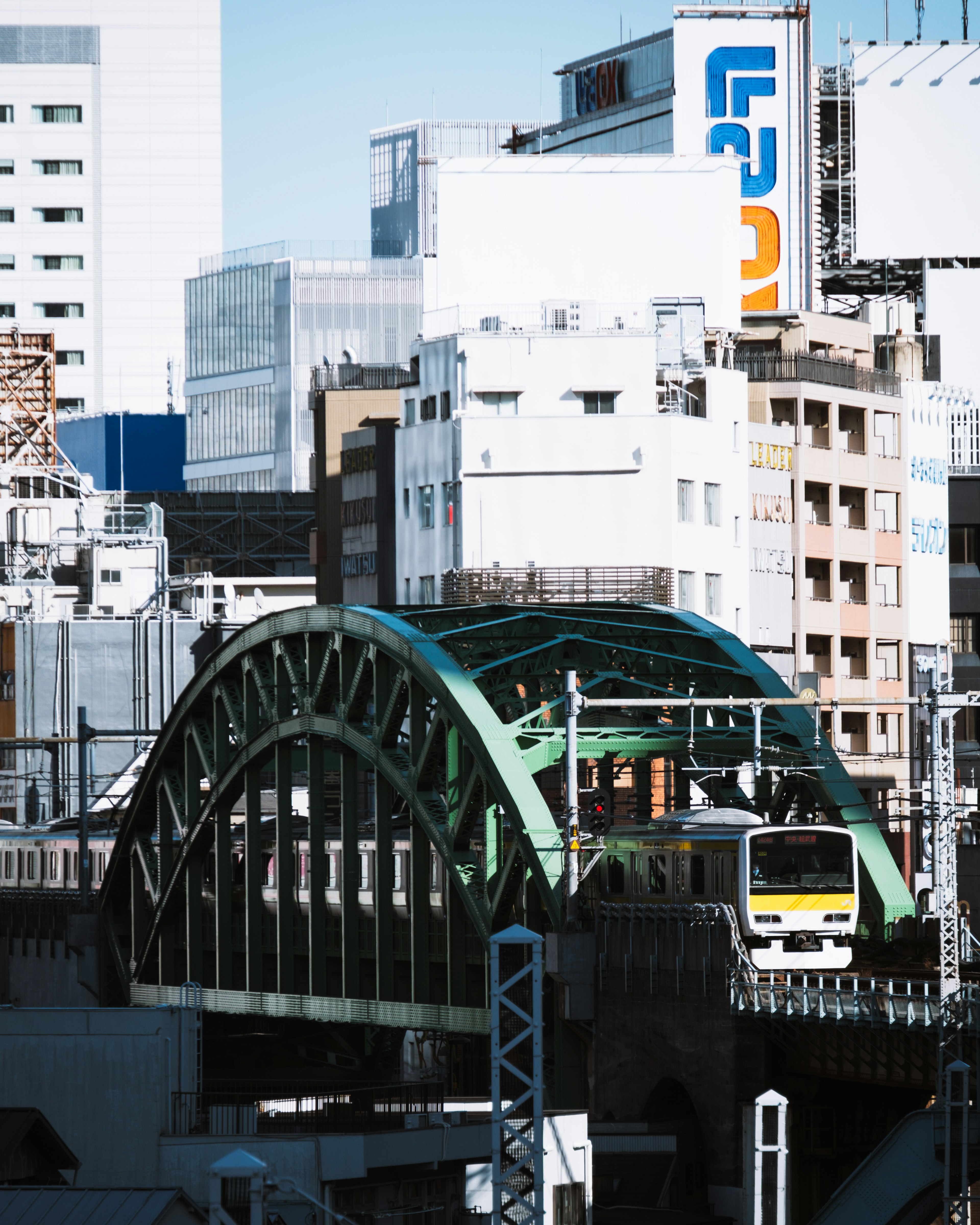 Train crossing a green arch bridge with surrounding skyscrapers