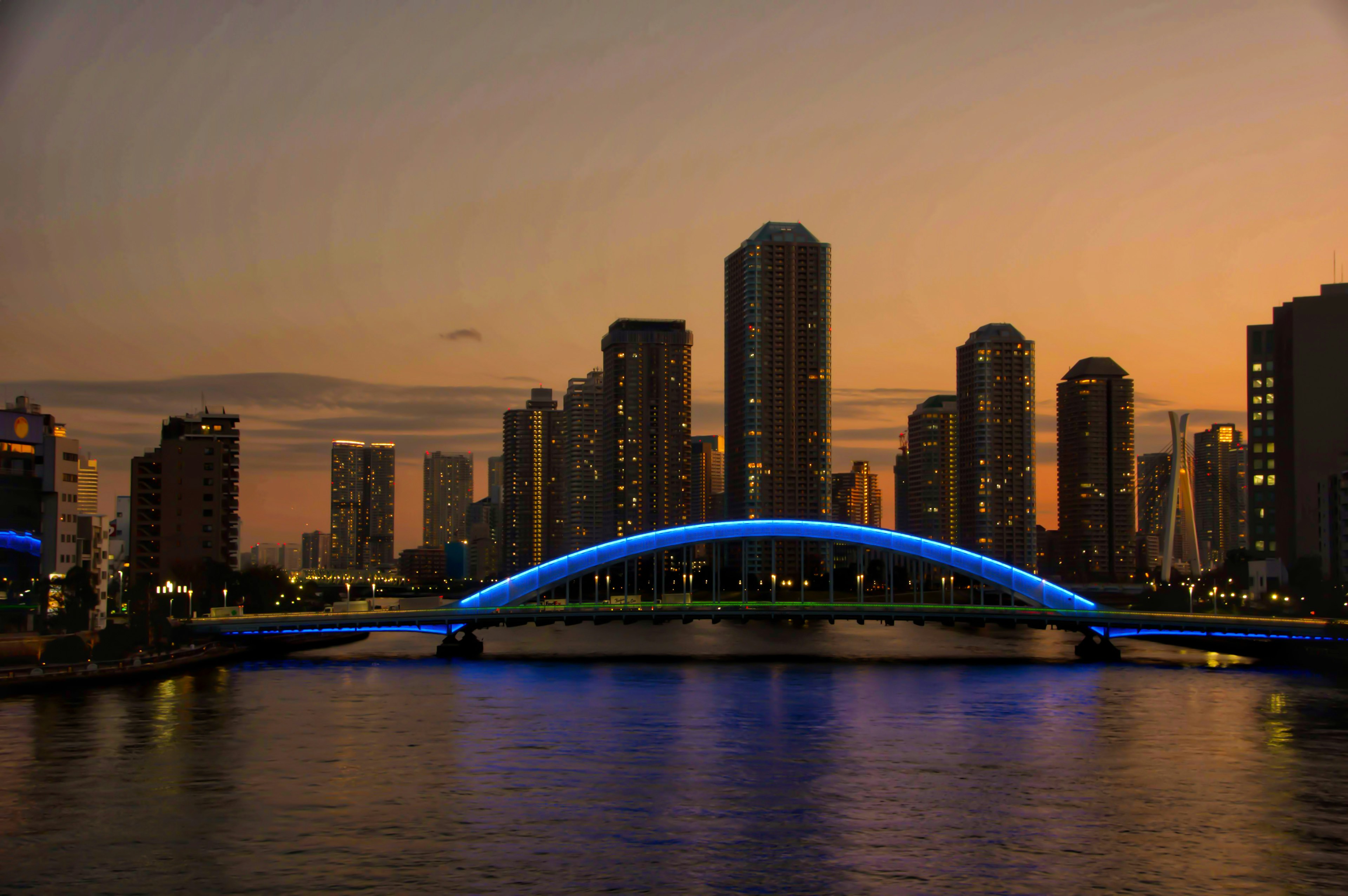 Silhouette de la ciudad al anochecer con un puente de arco azul