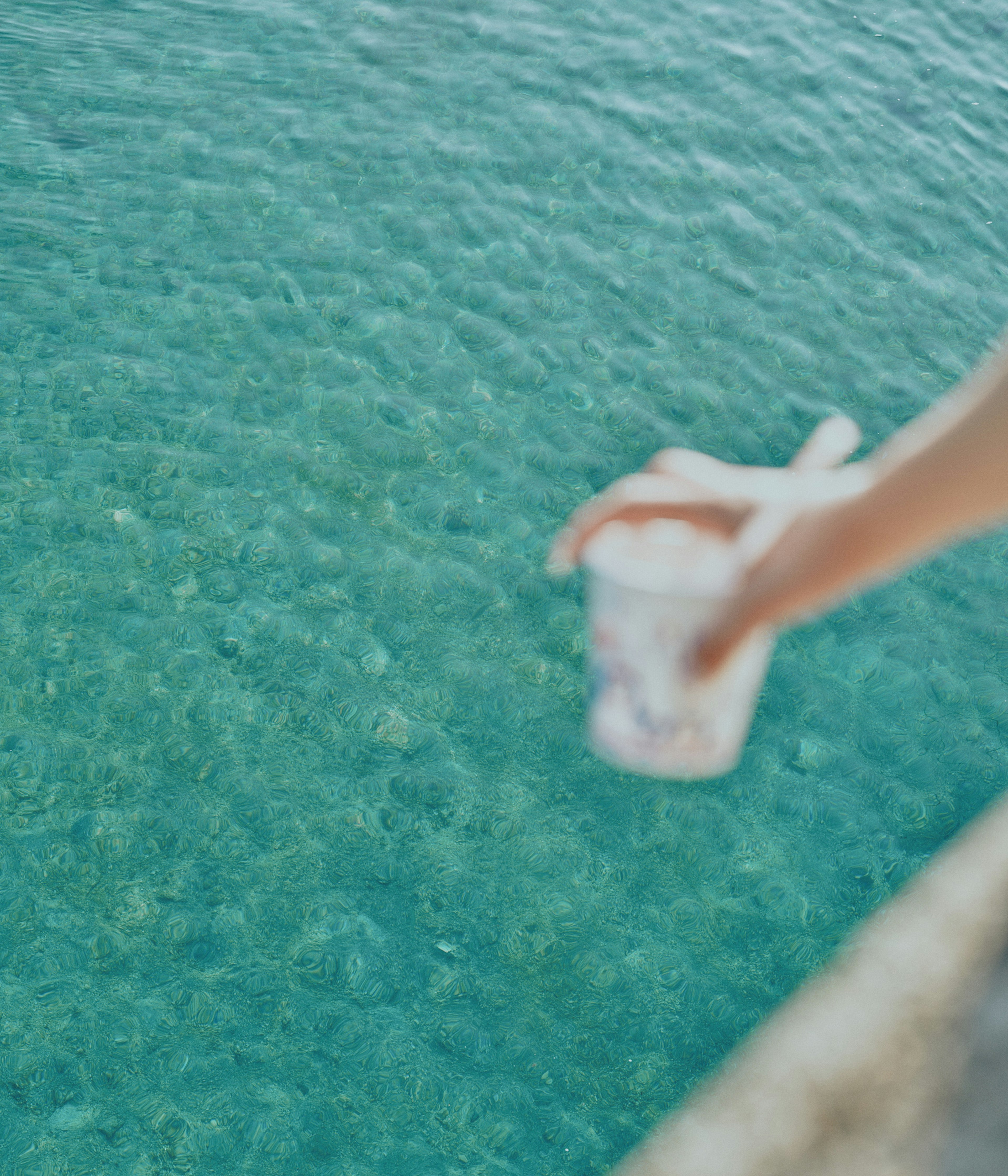 Una mano che tiene un bicchiere sopra una superficie d'acqua chiara