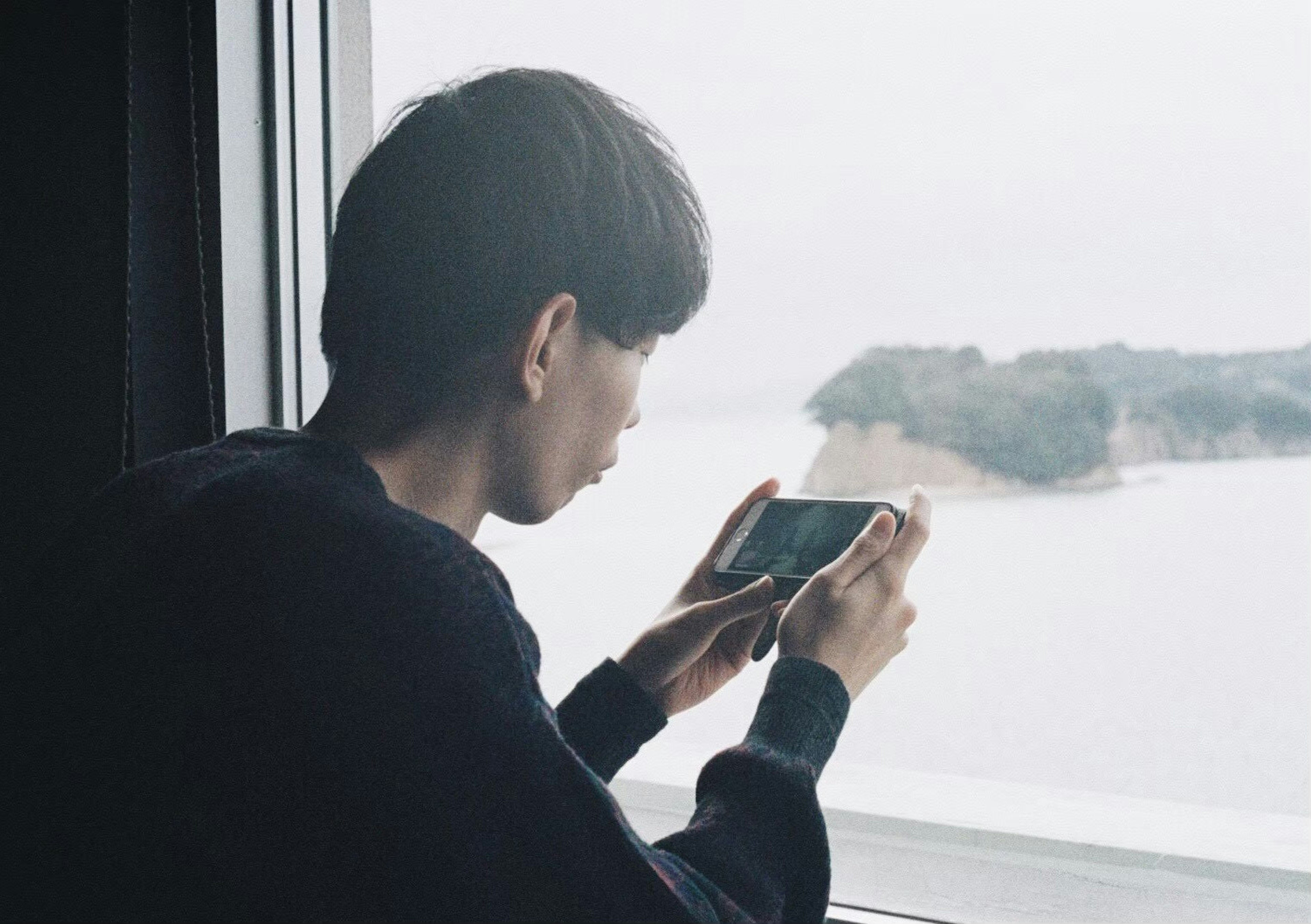 Joven tomando una foto con un smartphone mientras mira por la ventana