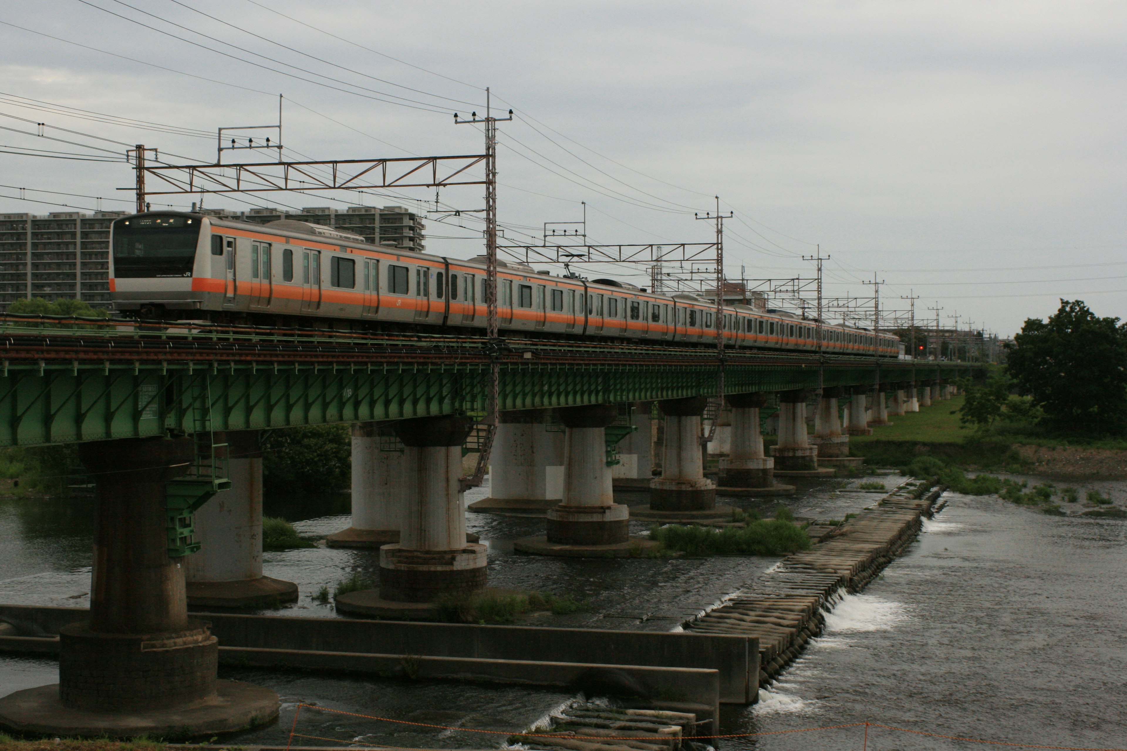 Kereta melintasi jembatan di atas sungai dengan langit mendung