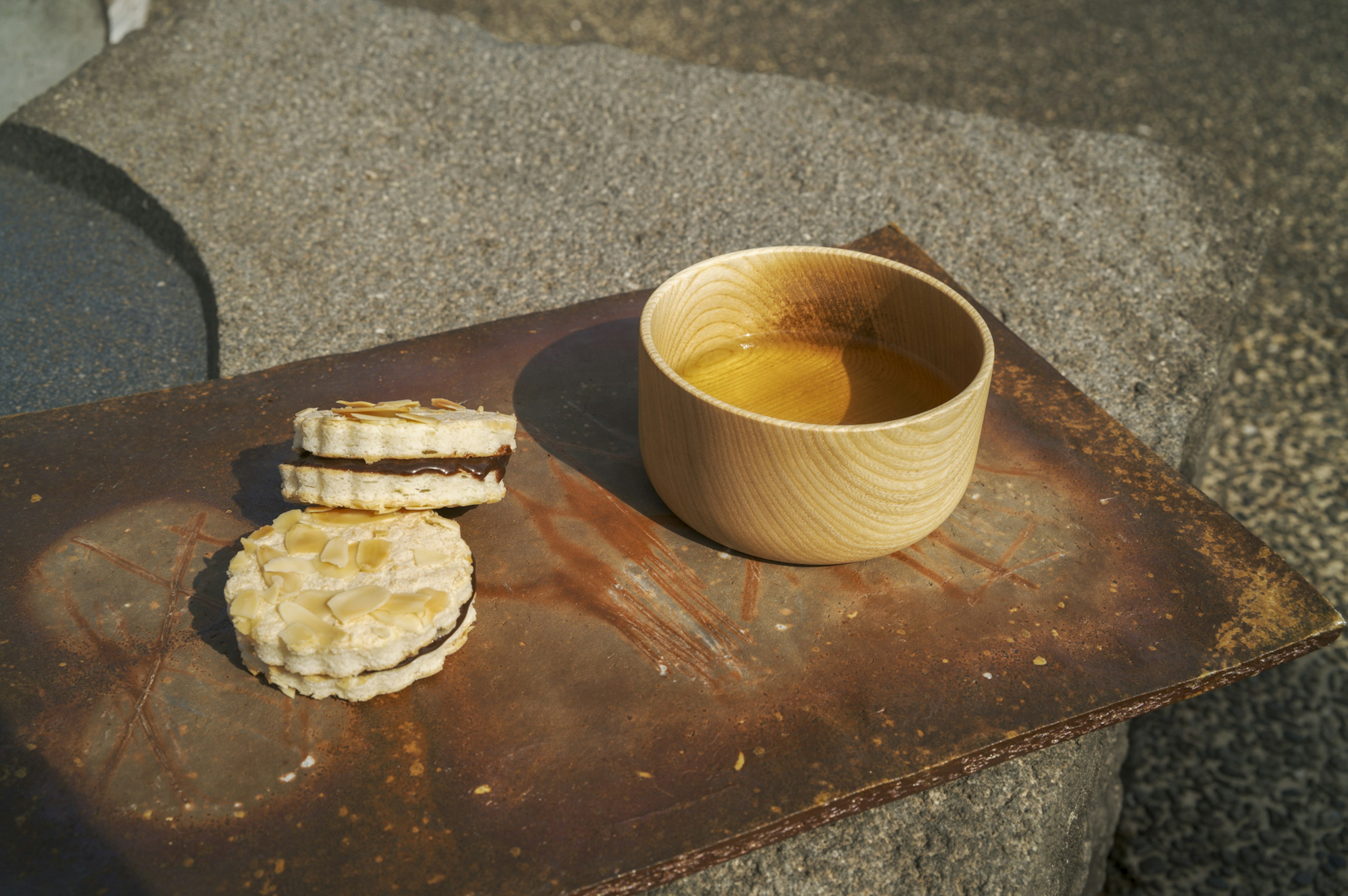 A wooden bowl with a drink next to two cookies on a metal surface