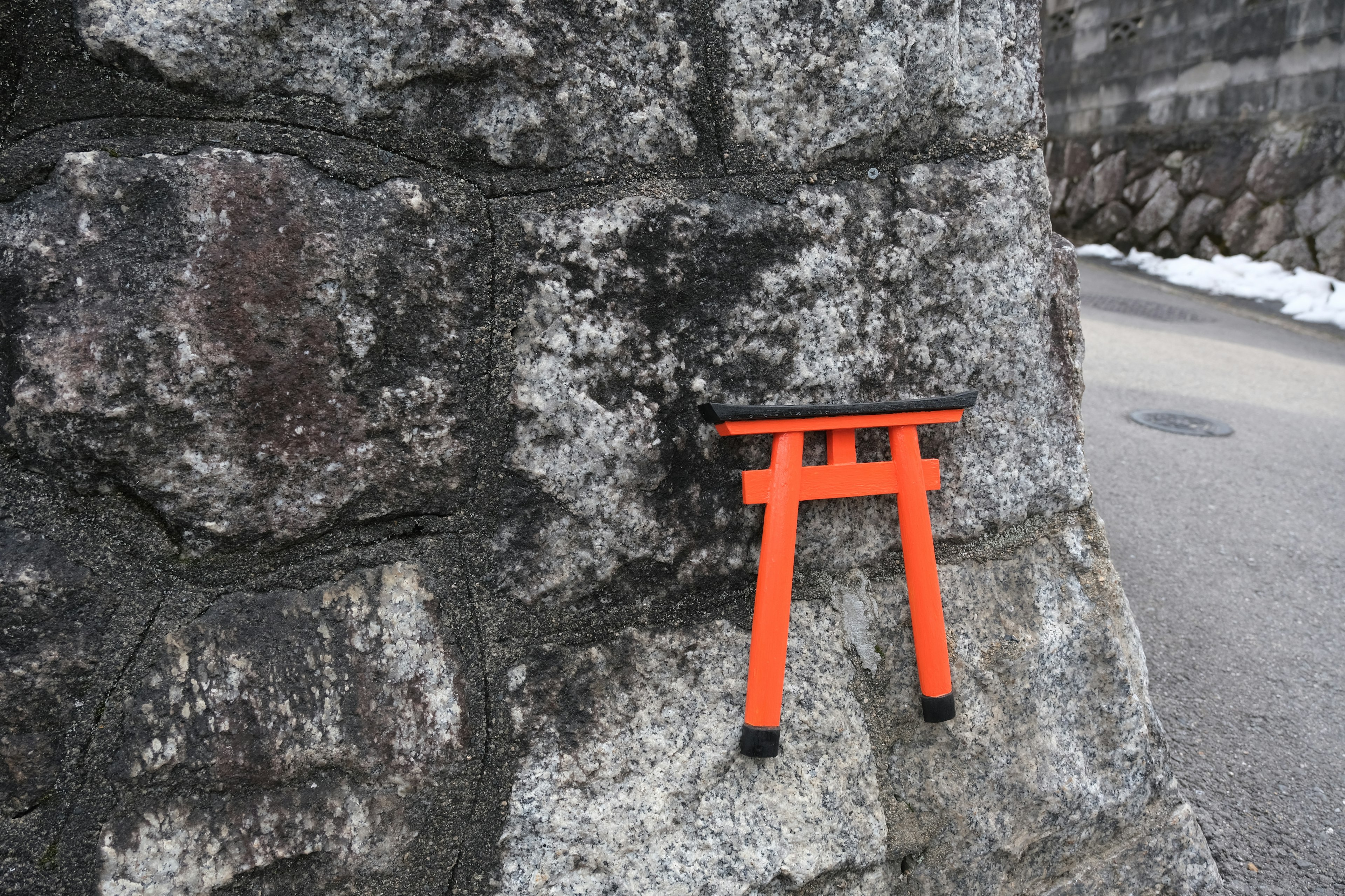 Small orange torii gate mounted on a stone wall