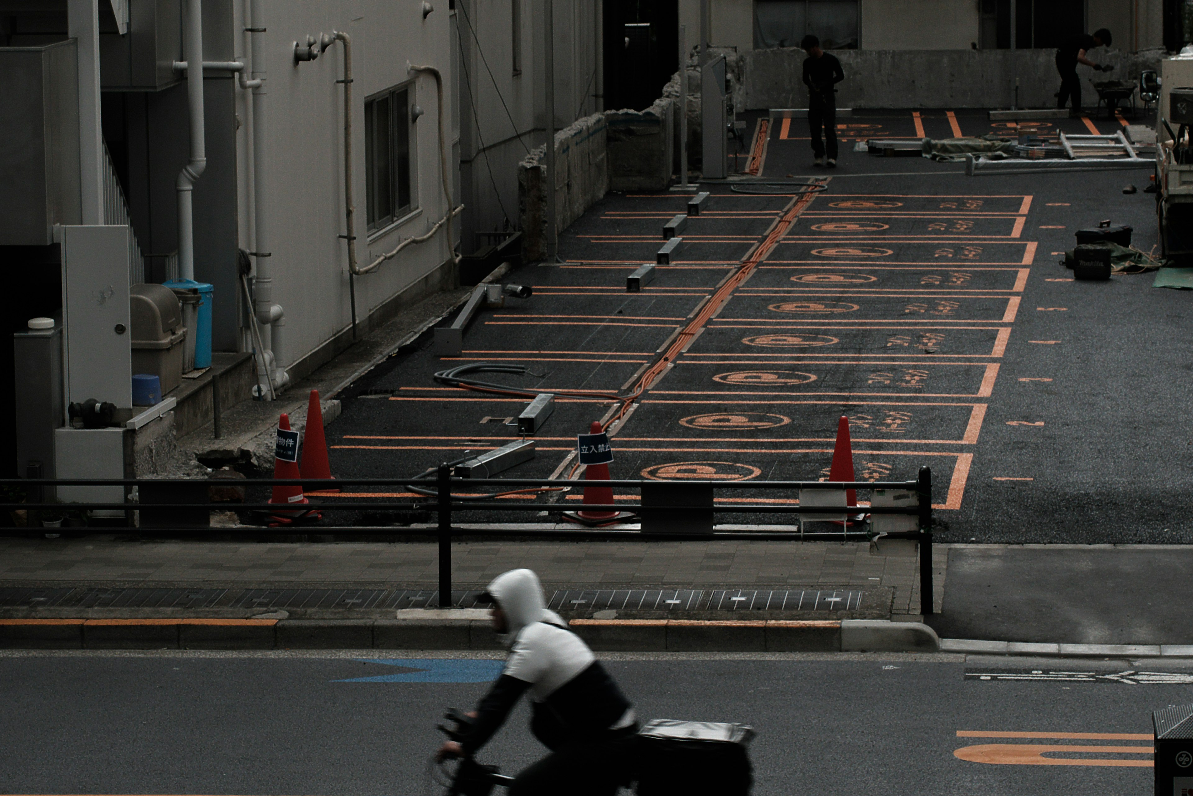 Delivery person riding a bicycle near construction area with parking spaces